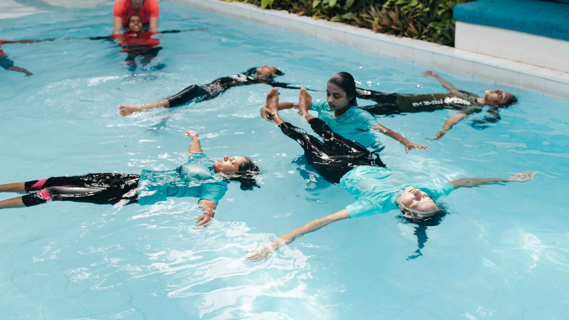 People float on their backs in a pool as they learn to swim.