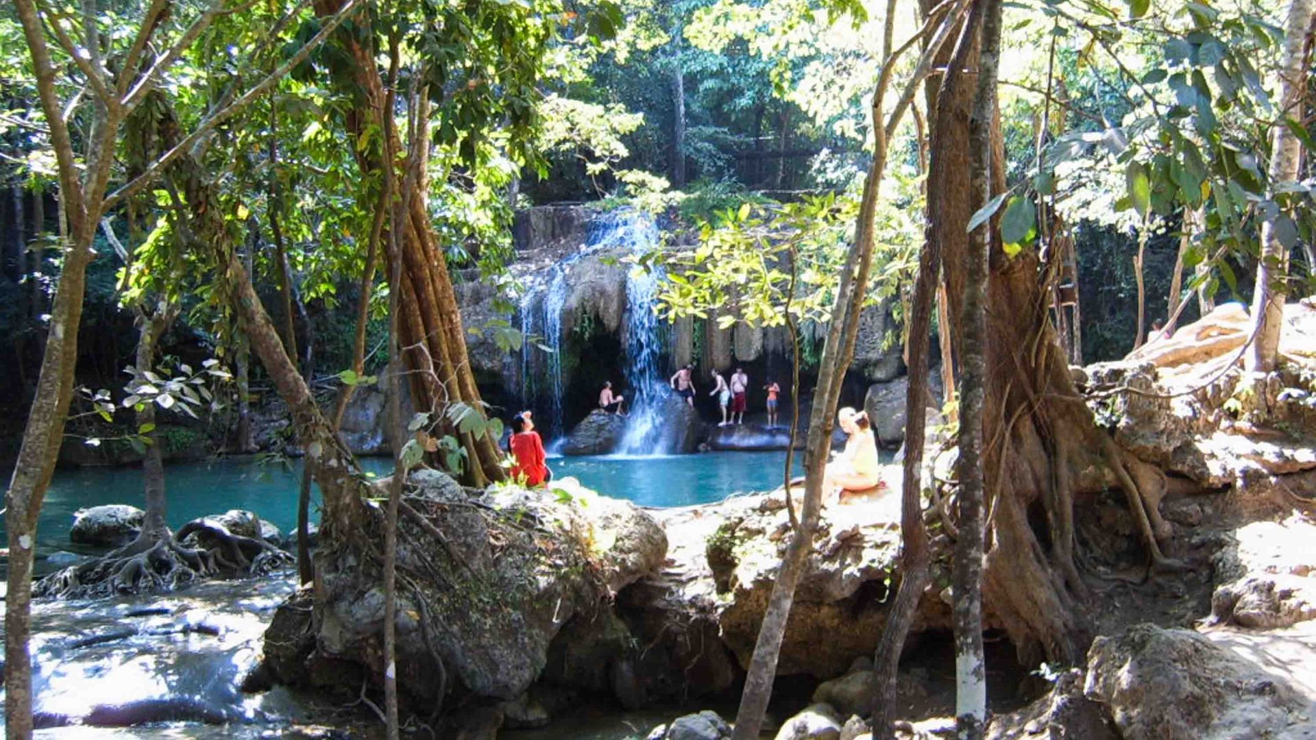 A blue waterfall with people at it, seen through the trees.