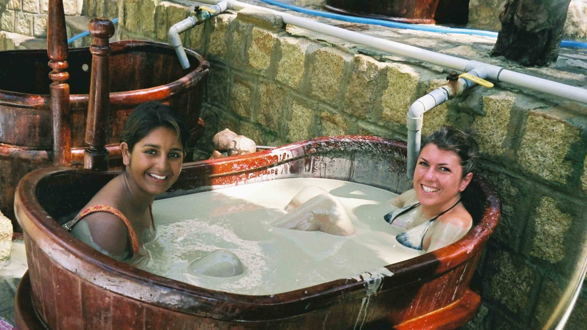 Two women sit in a bath of mud.