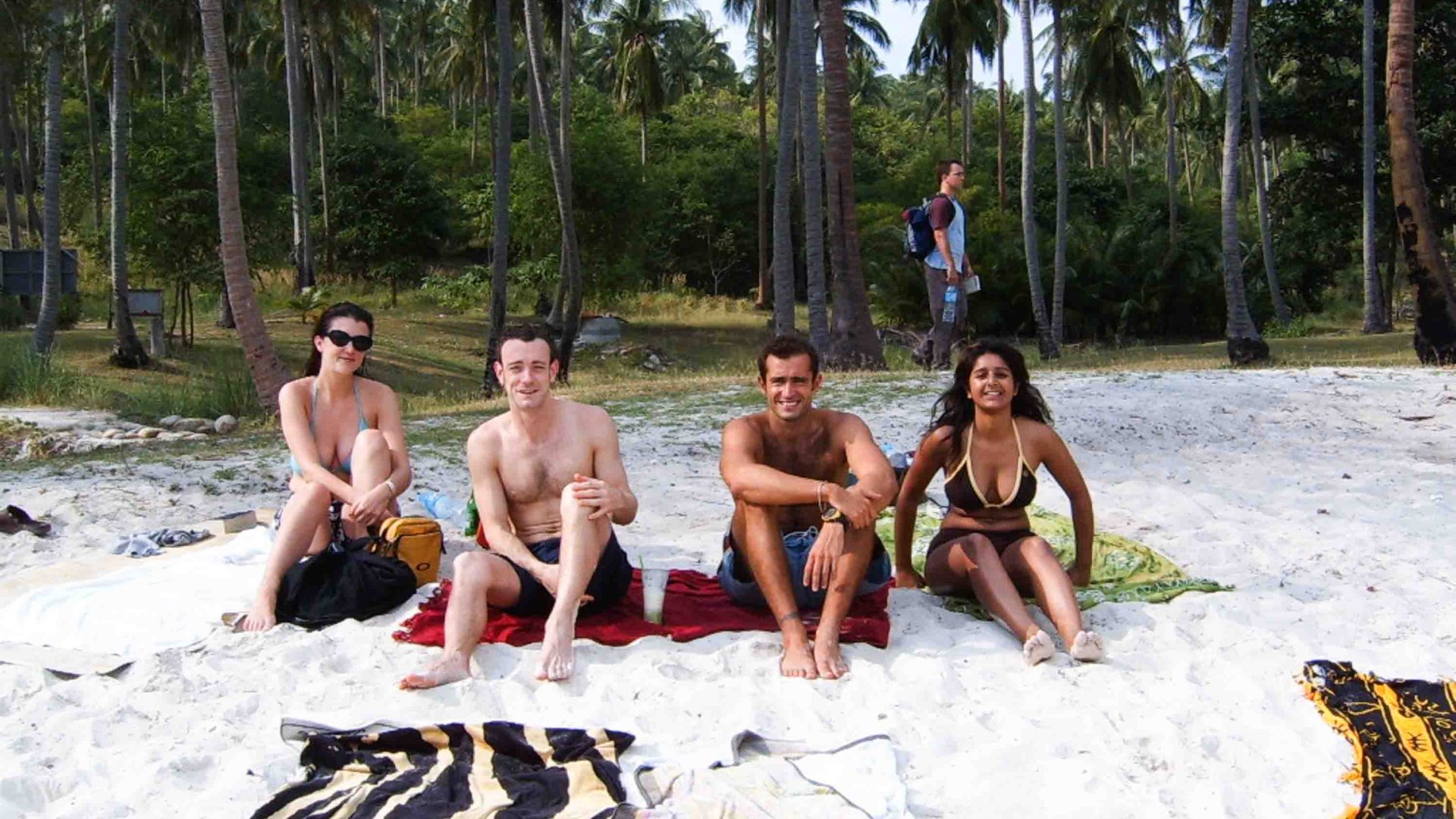 Four friends sitting on beach towels on a beach.