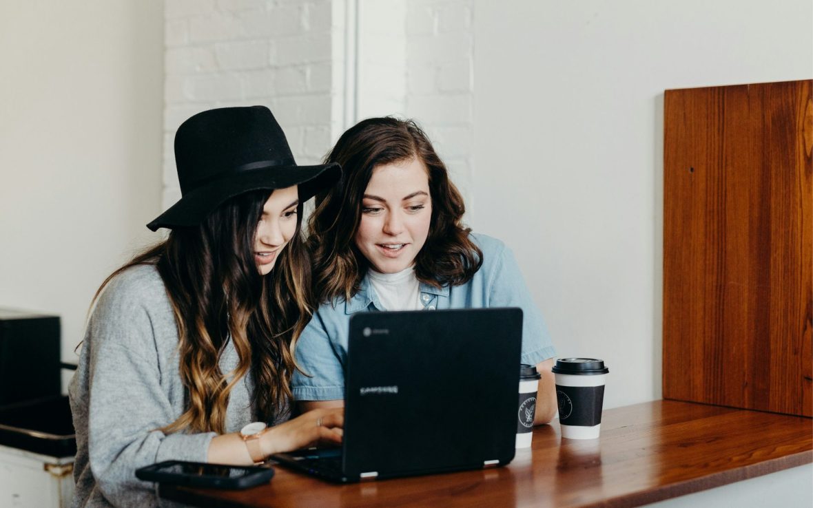 Two girls sat at a table with a laptop