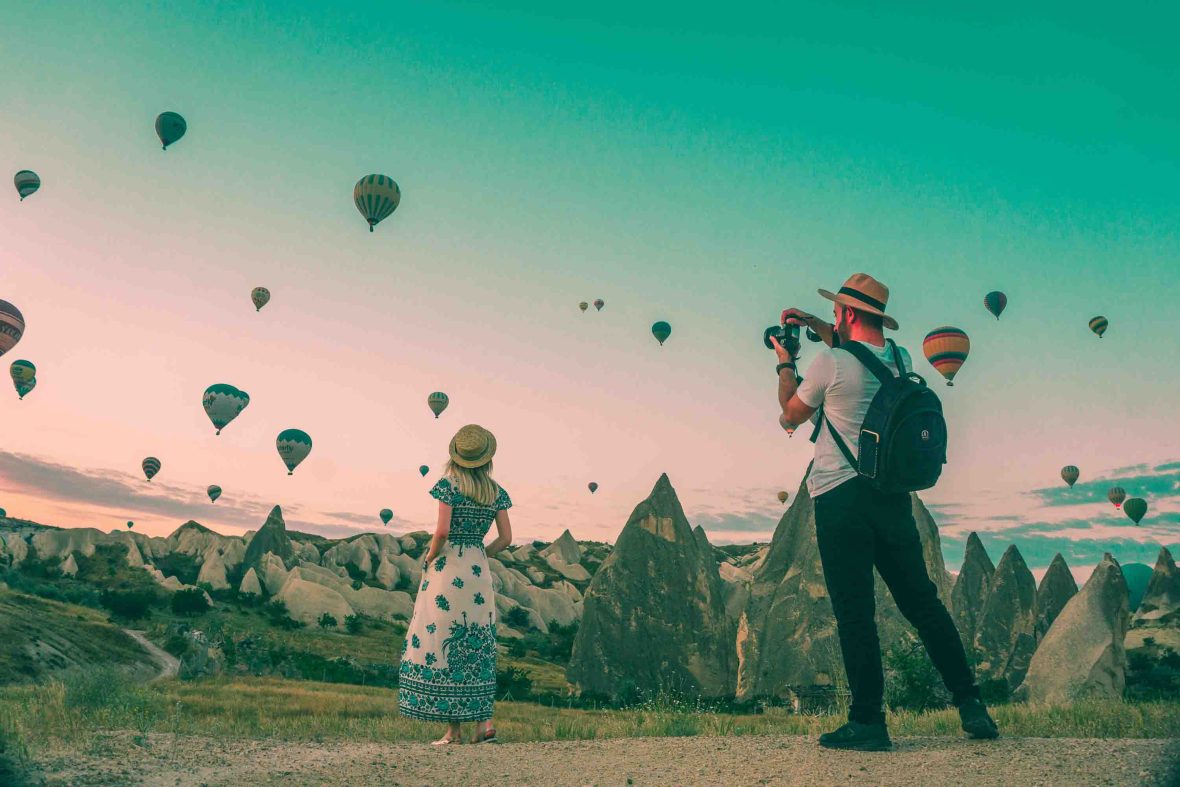 A woman is photographed by a man as she is looking at hot air balloons rising above the 'fairy chimneys'.