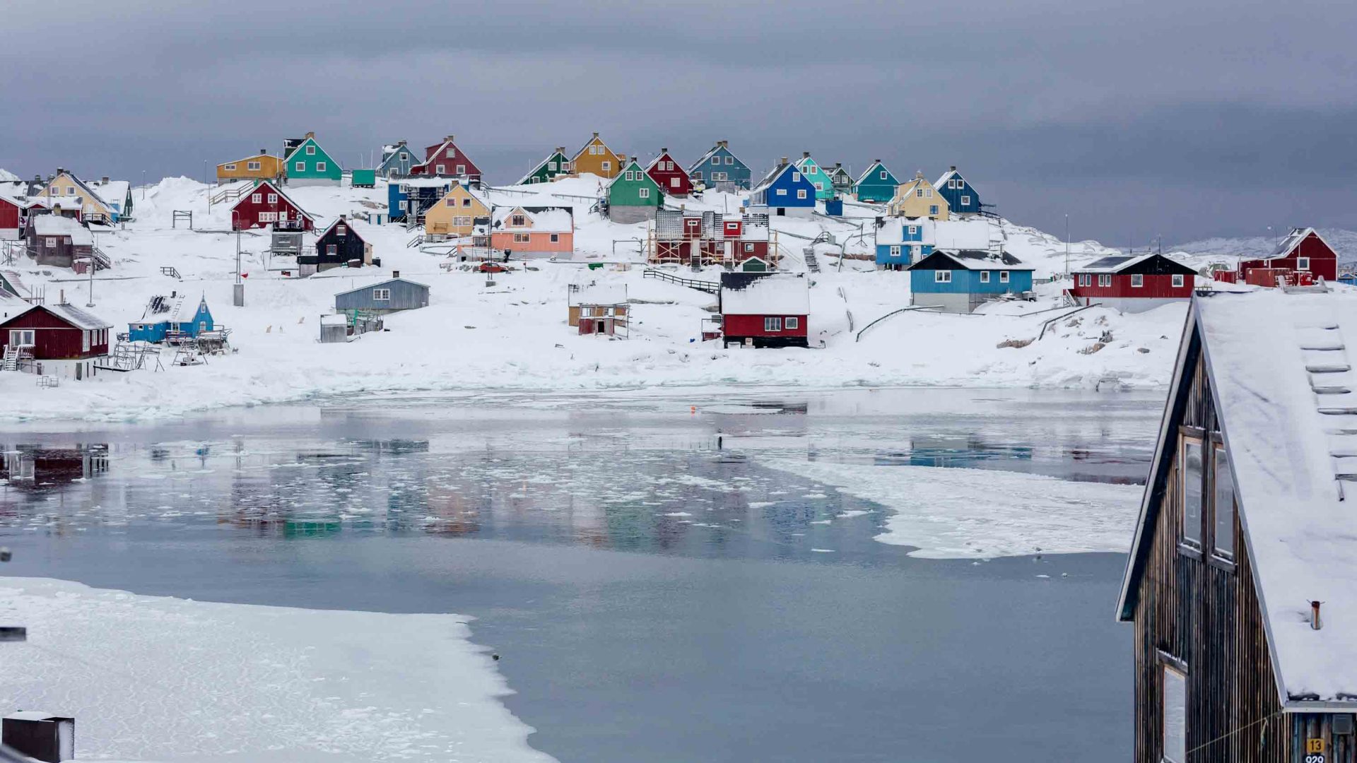 Colourful houses dot a snowy landscape alongside some icy water.