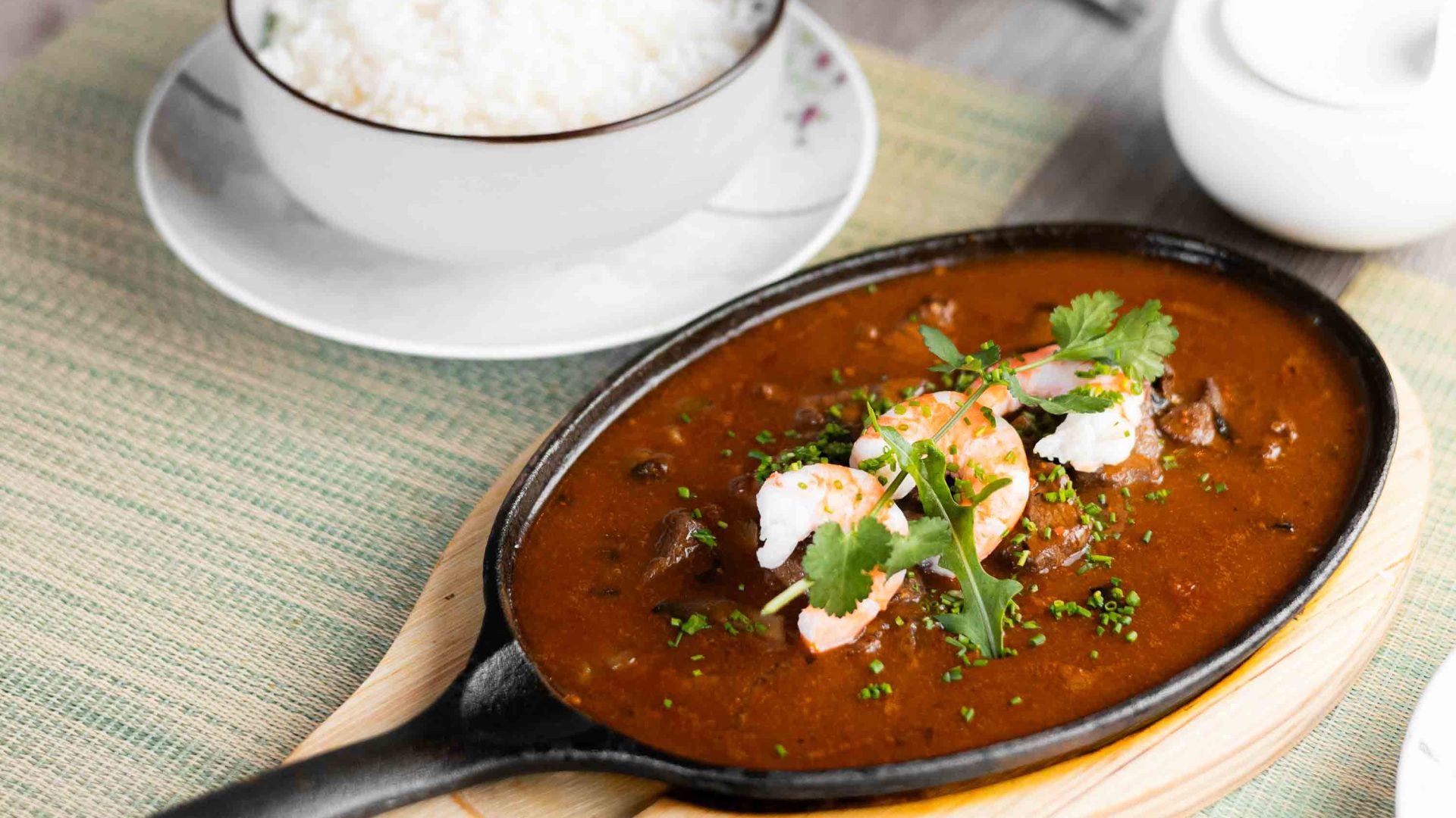 A stew on a dish with a bowl of white rice next to it.