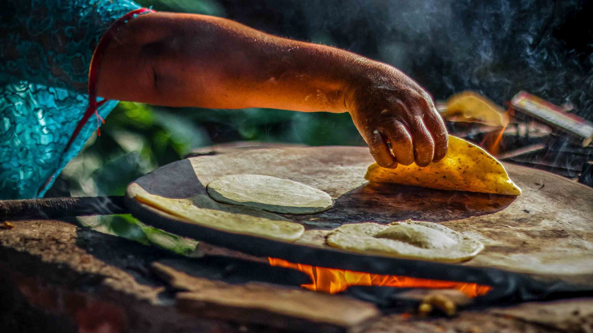 Hands can be seen preparing memelas over a fire.