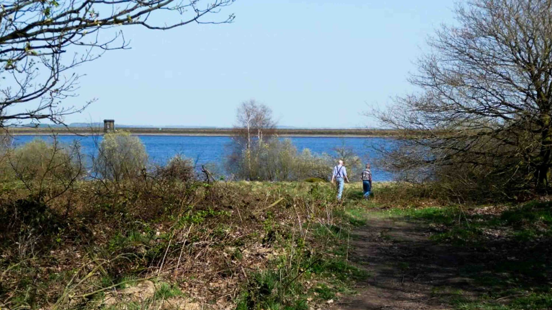 Two people walk along a trail toward a reservoir.