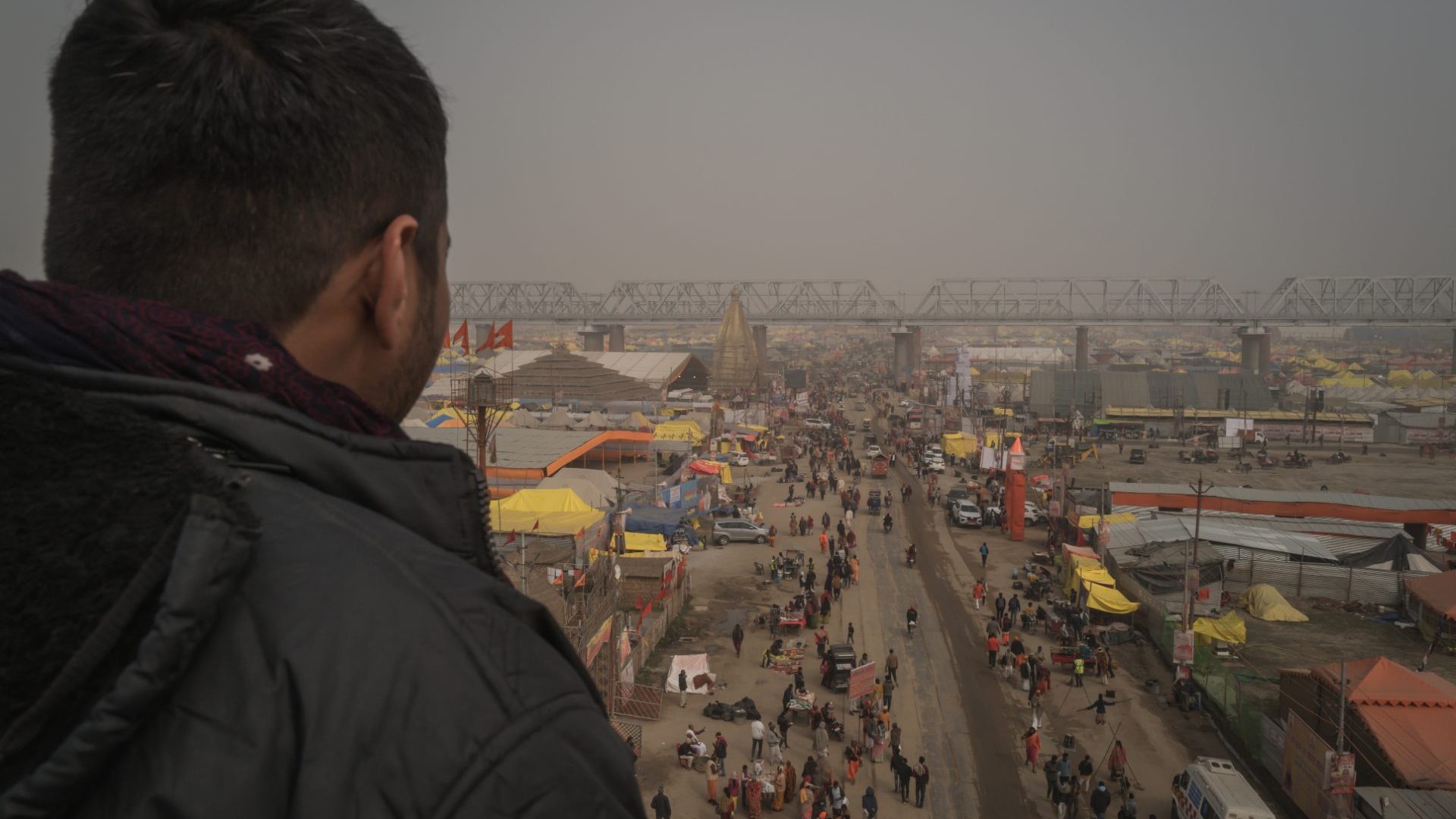 Young Indian man looks out over the festival from bridge.