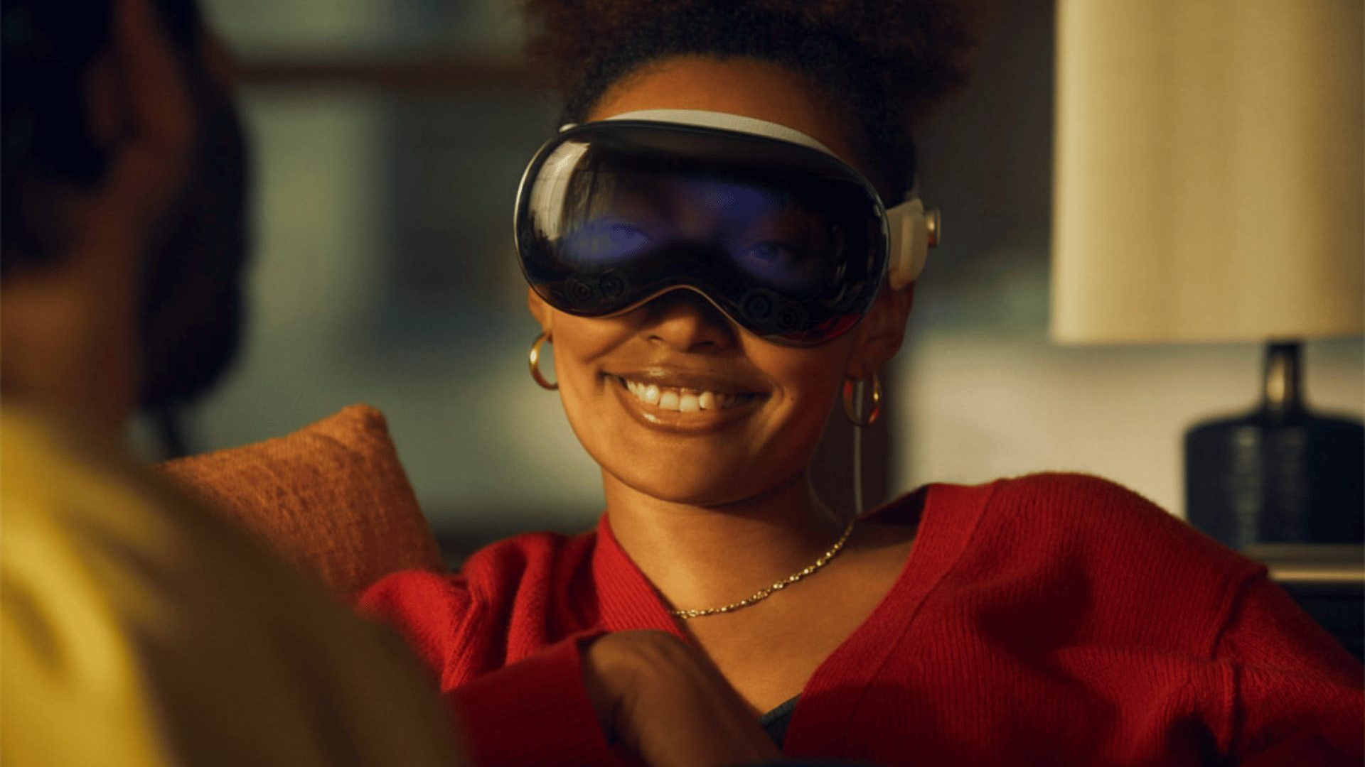 A woman sitting on a couch wearing a VR headset. Her eyes are visible in the screen.