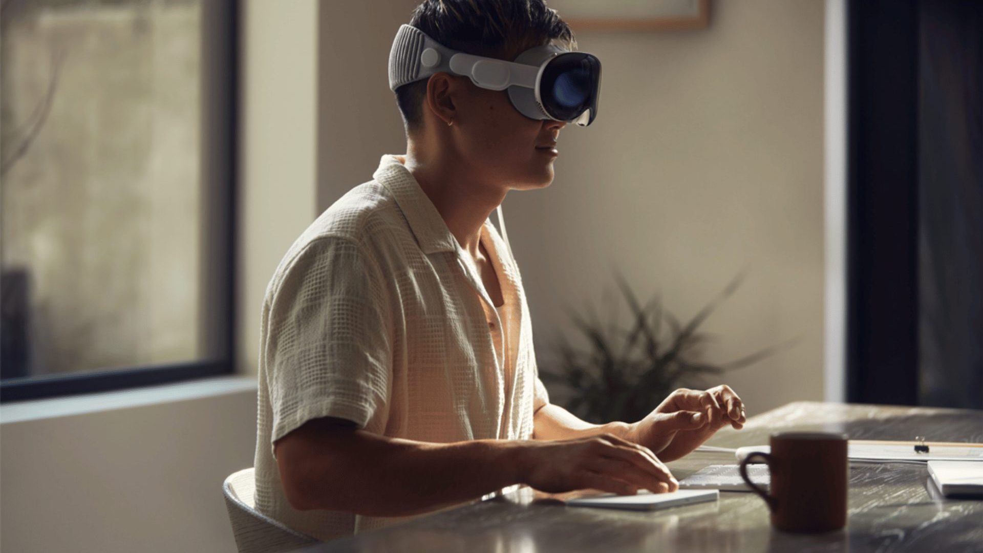 A side view of a person wearing the Apple Vision Pro while working at a desk.