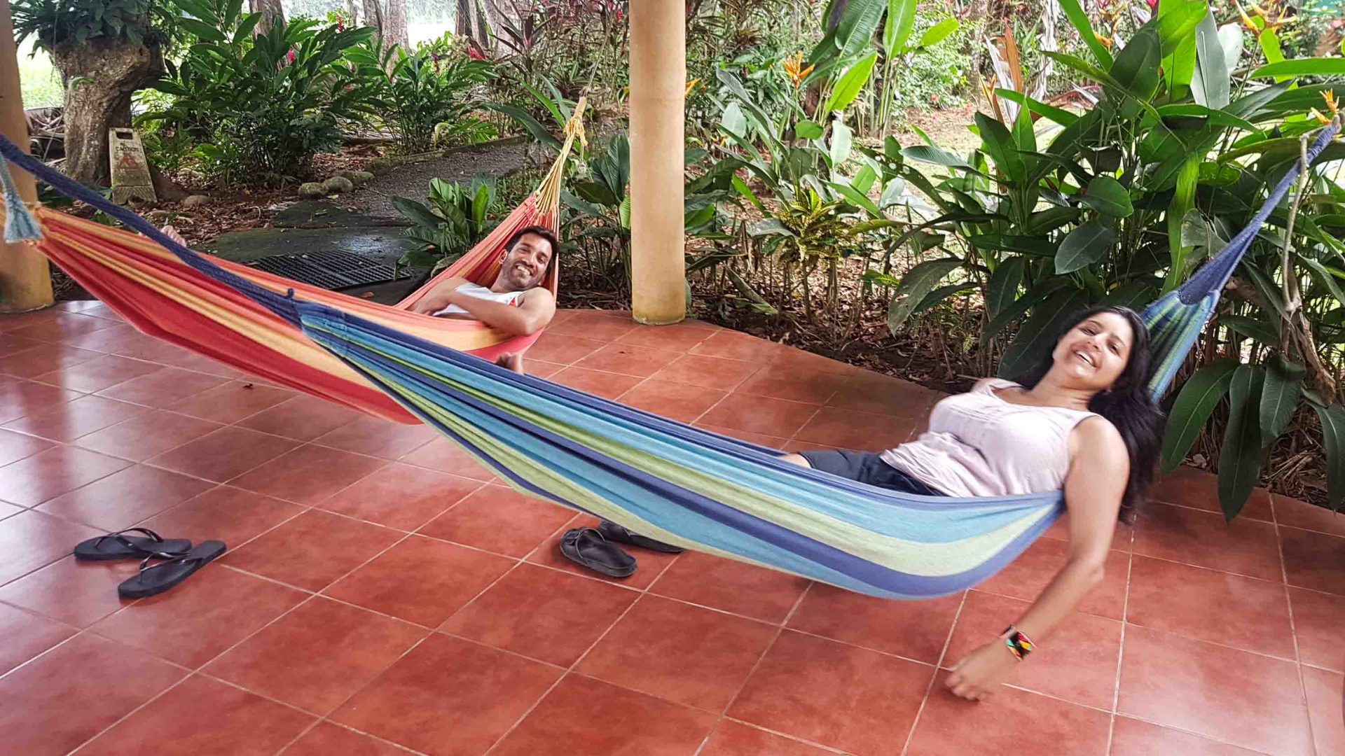 A man and a woman smile while lying in a hammock each.