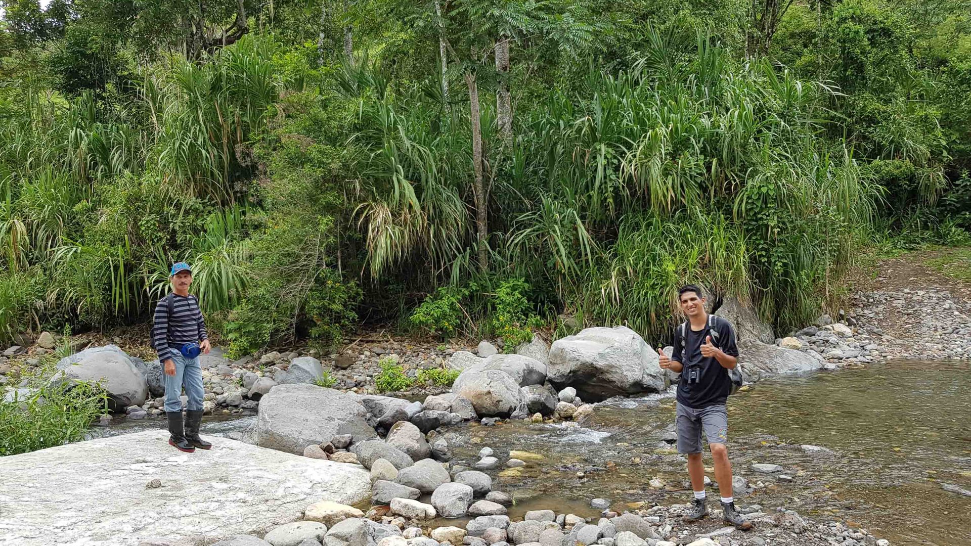 Two men stand in ankle deep river water.