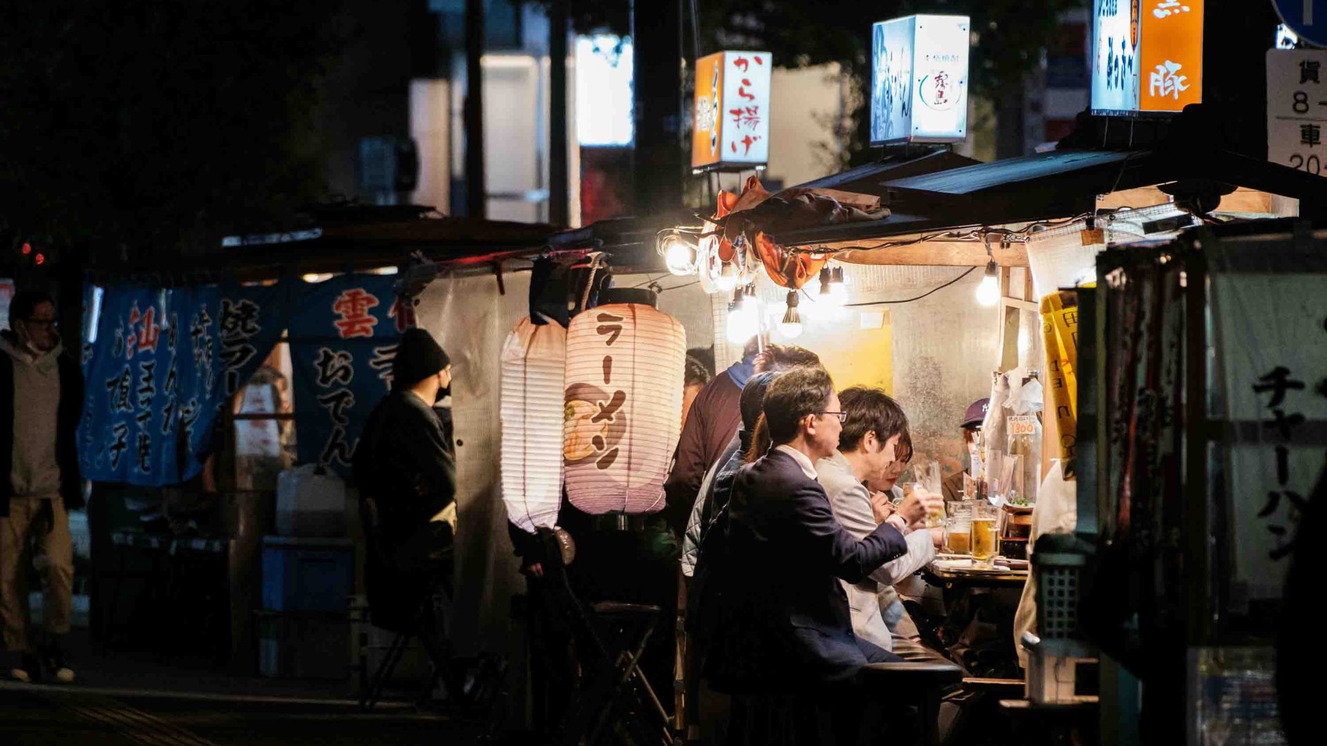 People enjoy food and drinks at a yatai at night.