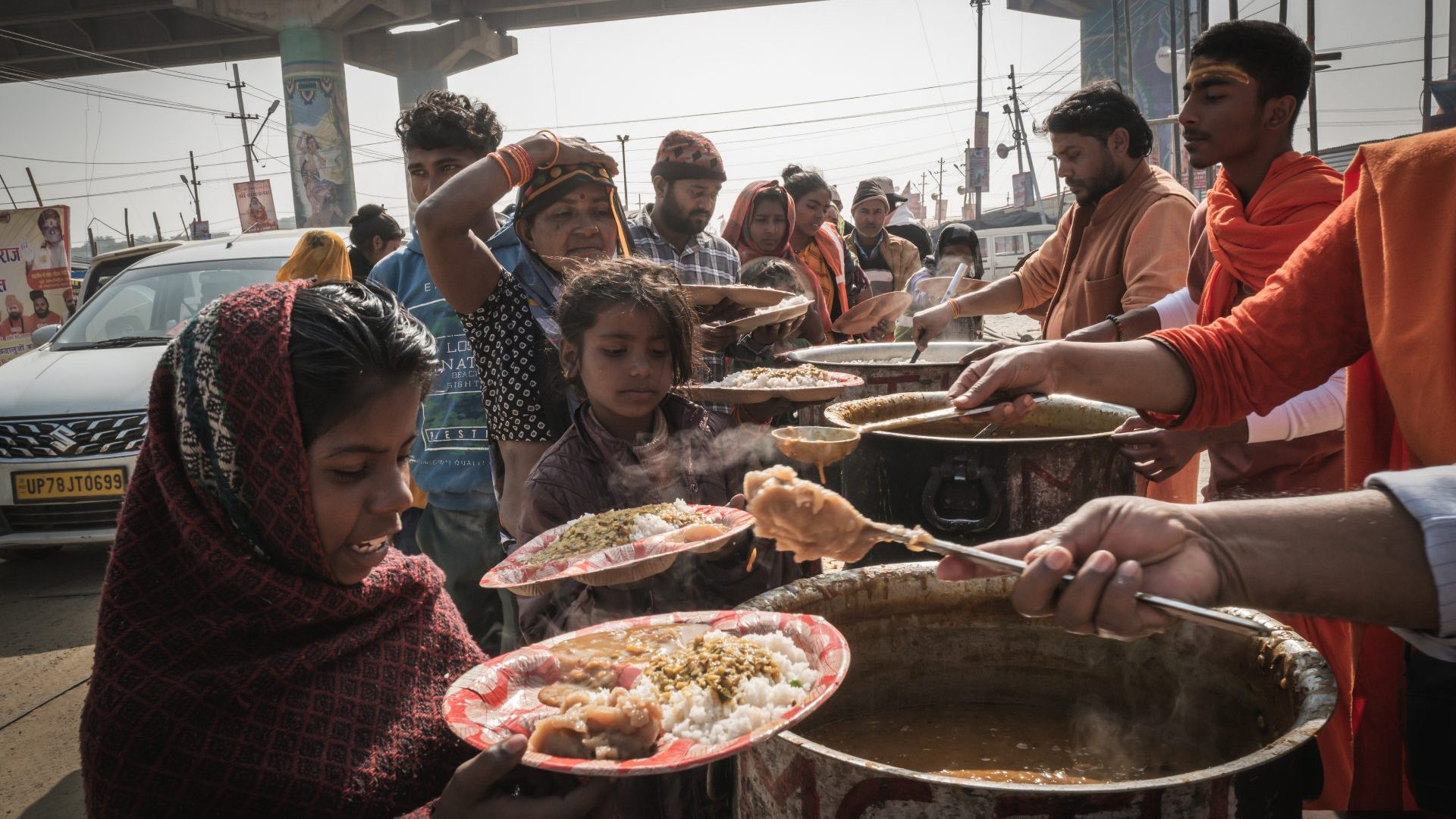 People being given food out of huge pots.