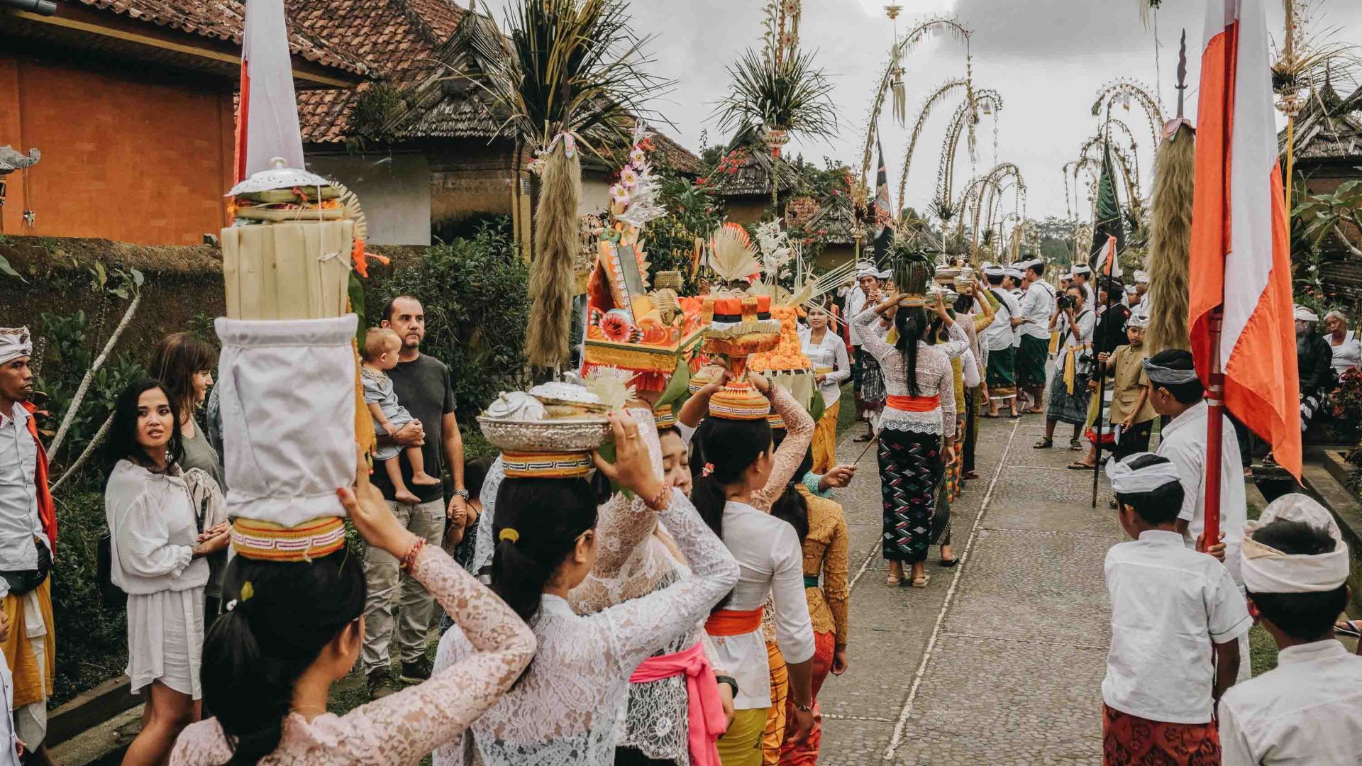 Tourists and locals watch a Balinese procession in the street.