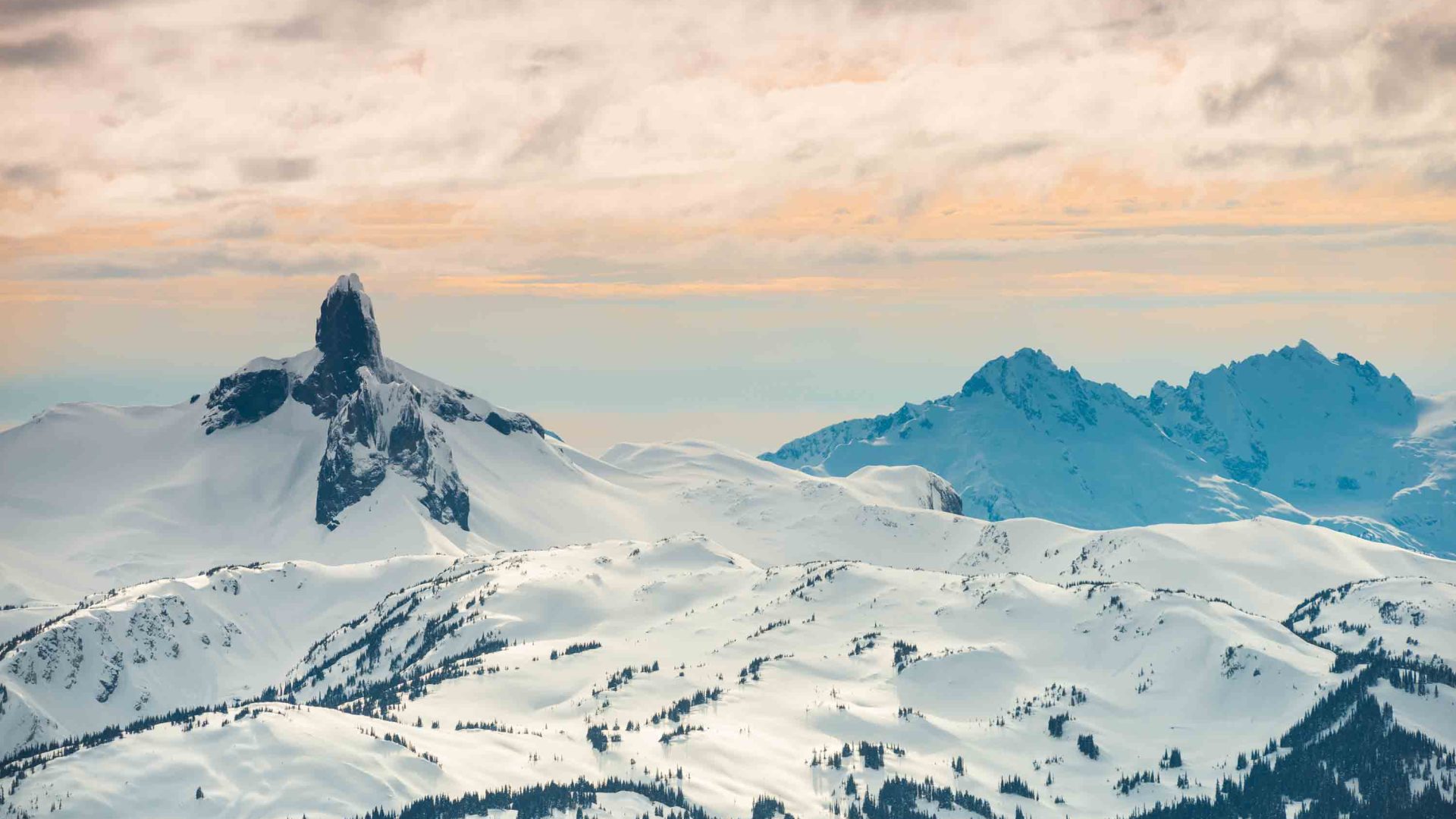 A black rocky outcrop juts out of the top of a snowy mountain.