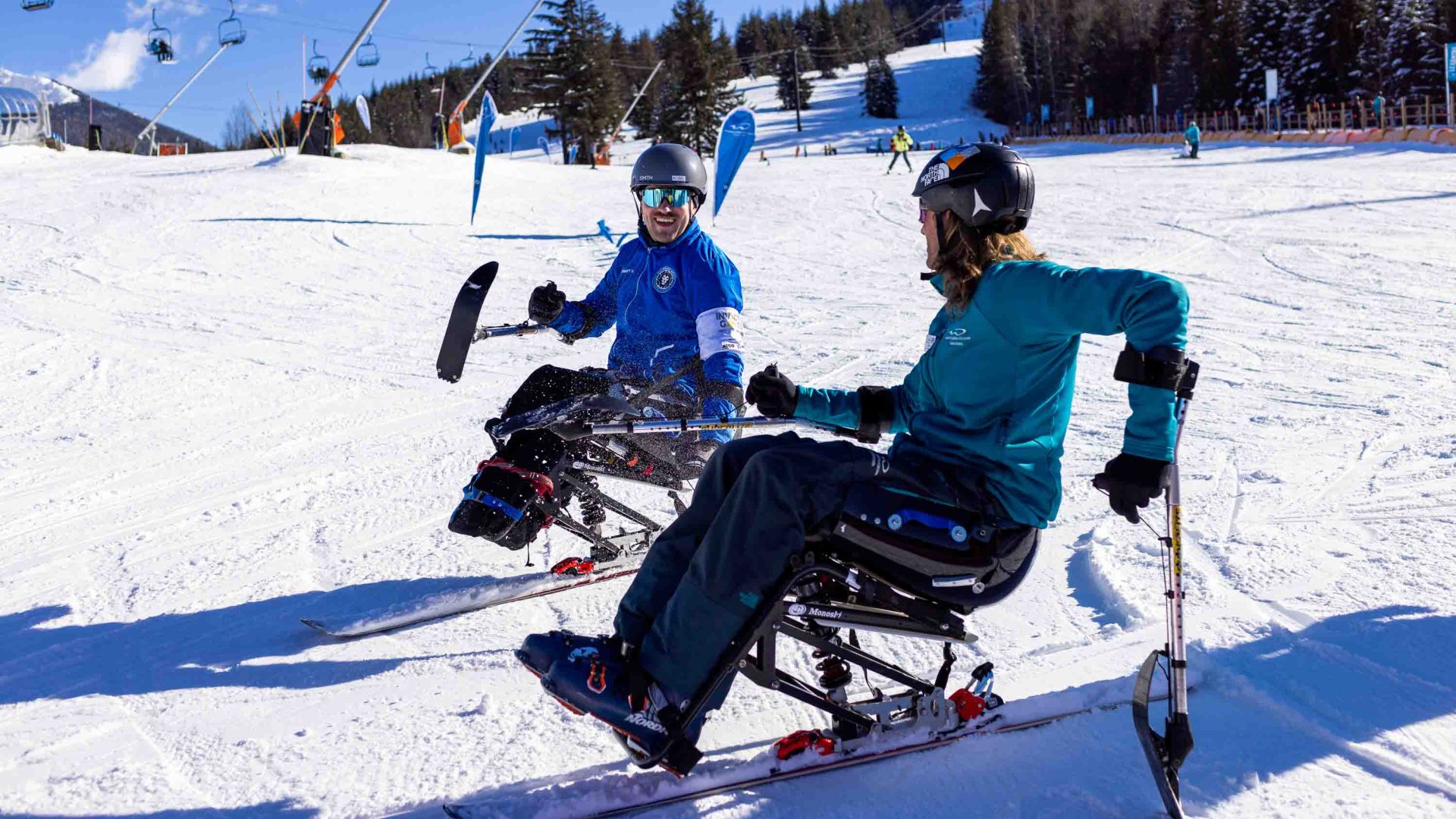 Two people on adapted skis on a ski slope.