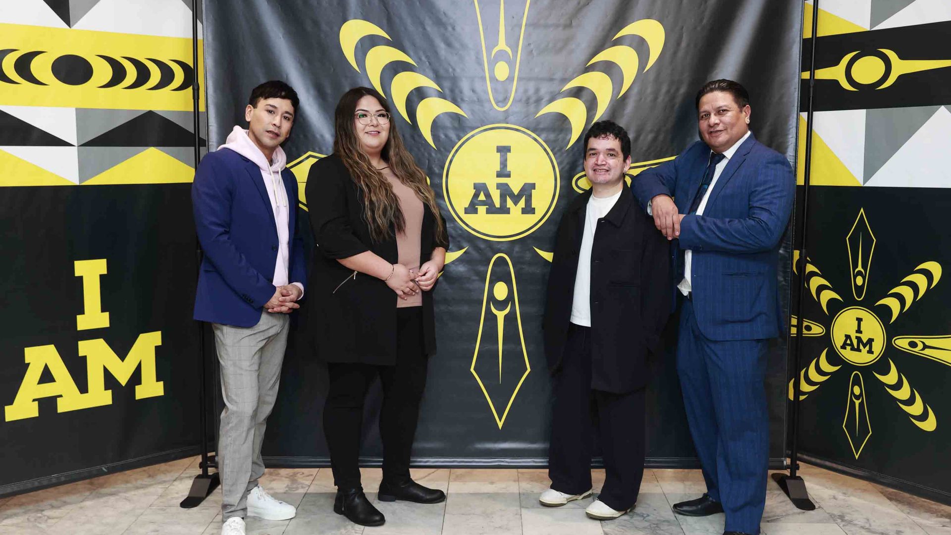 Four people stand in front of a banner of a black and yellow logo.