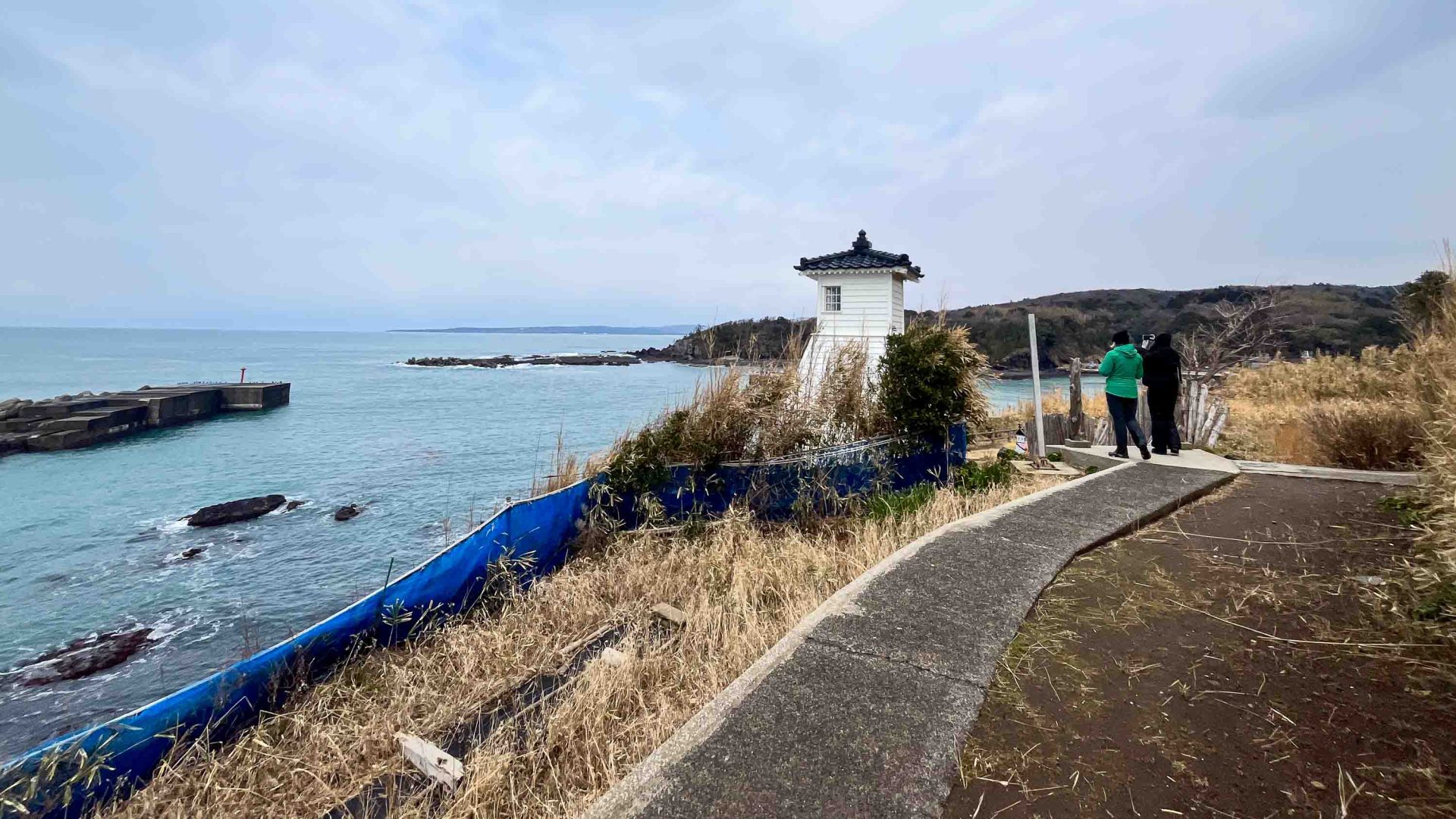 A path leads to a white lighthouse by the calm sea.