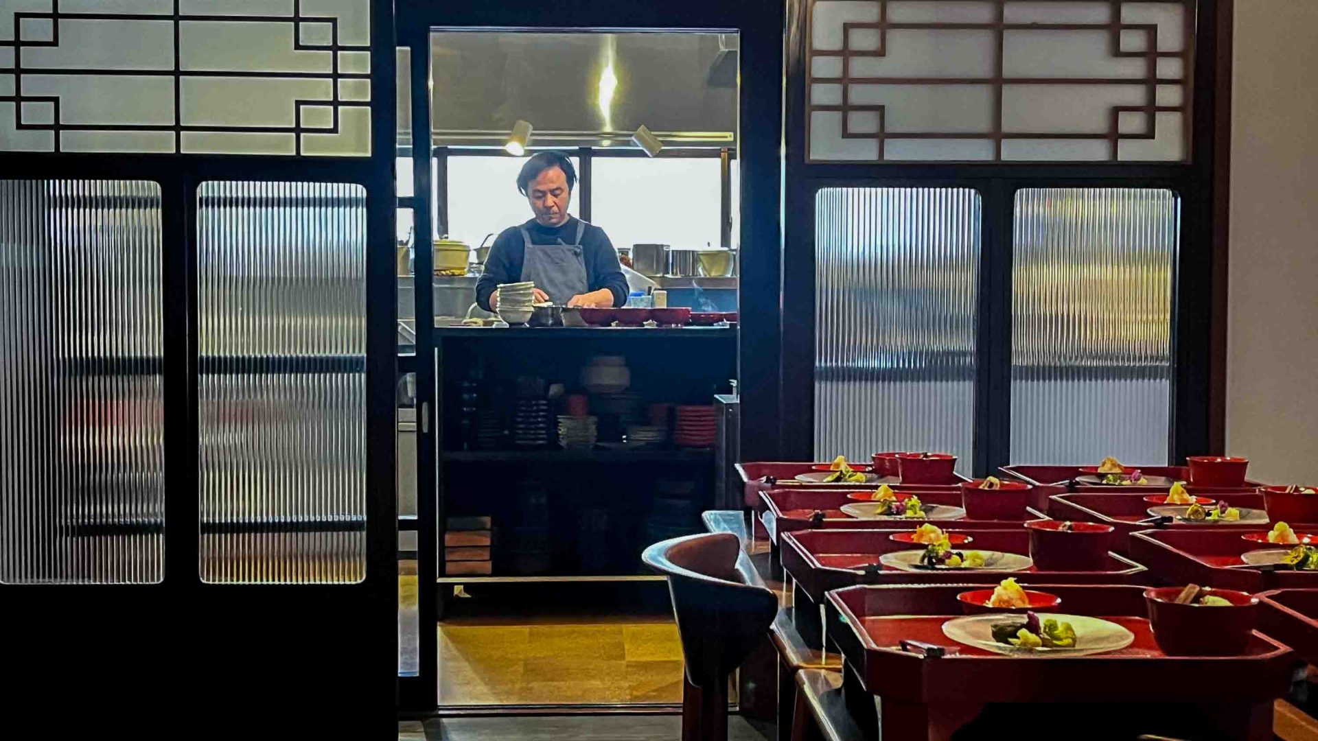 A chef works and some of his dishes are on a table in front of him.