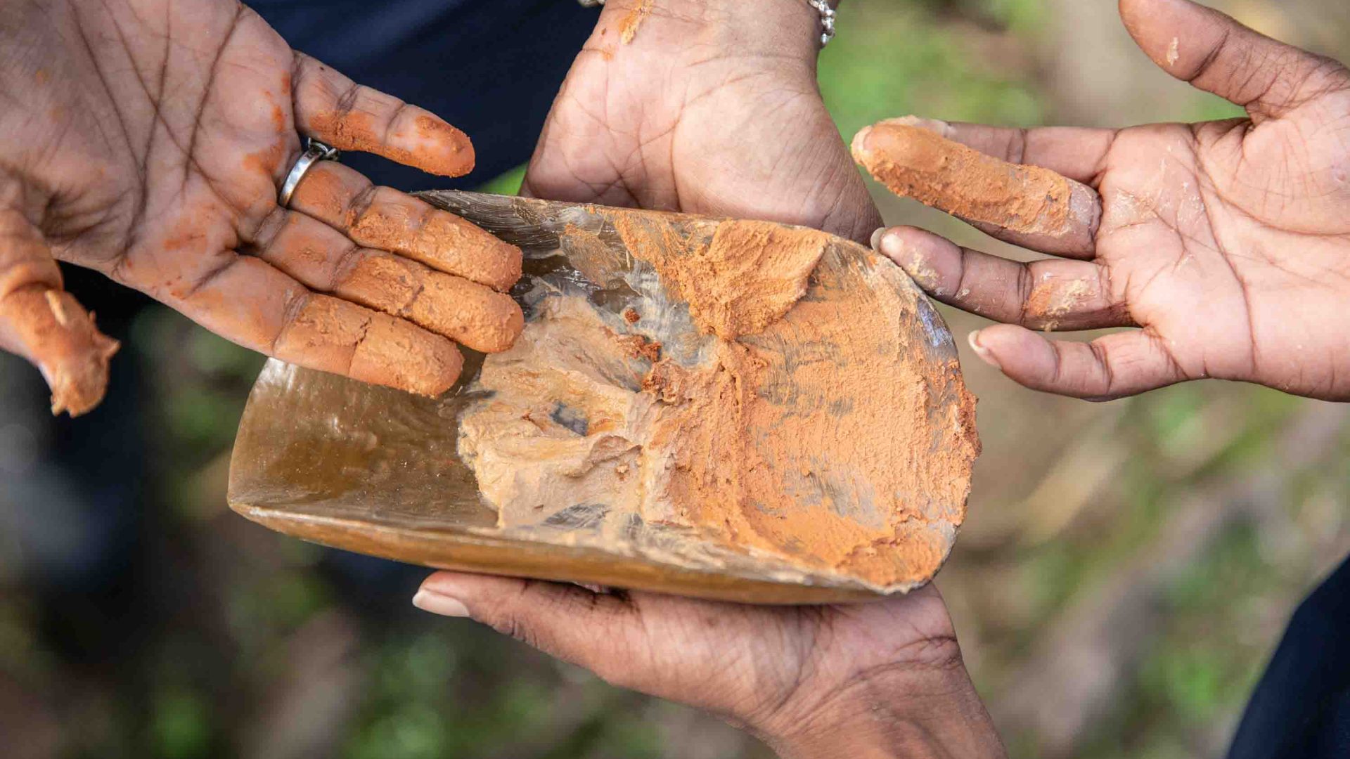 Fingers point to mud in a wooden dish.