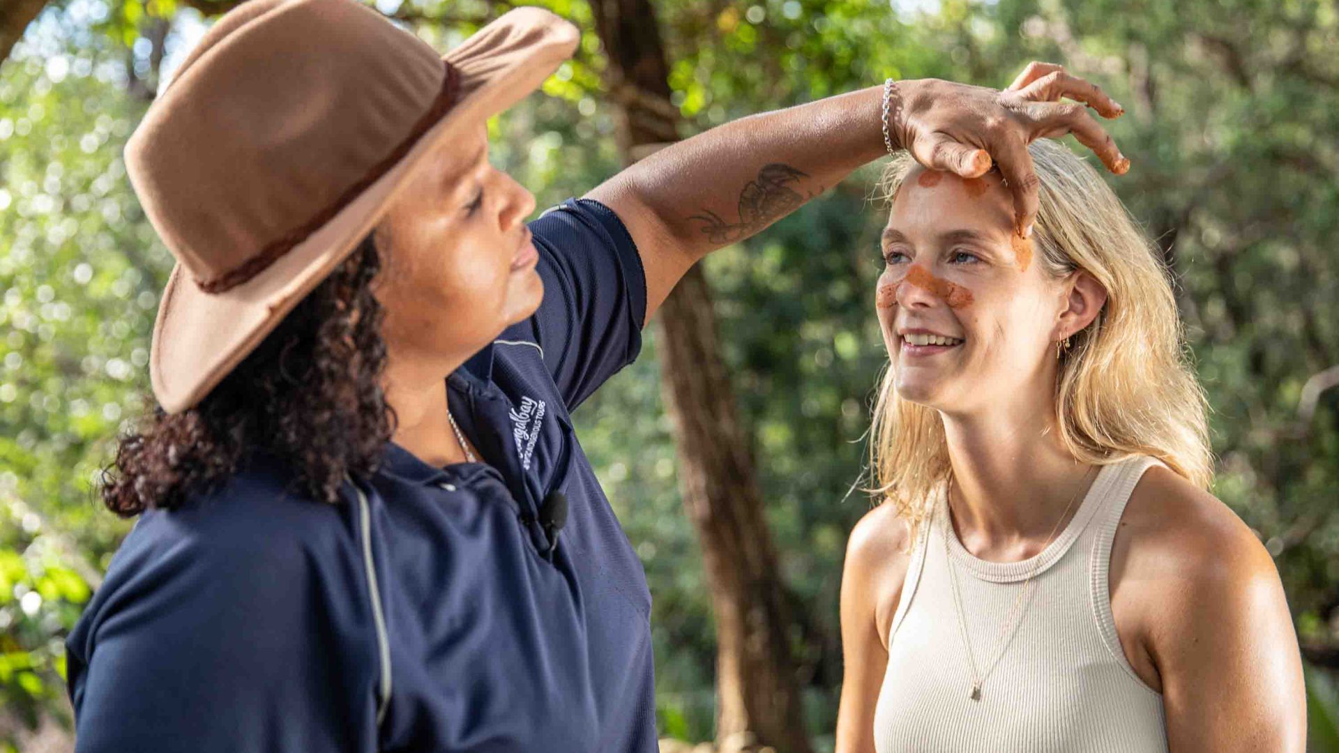 A woman puts a mud marking on another woman's face.