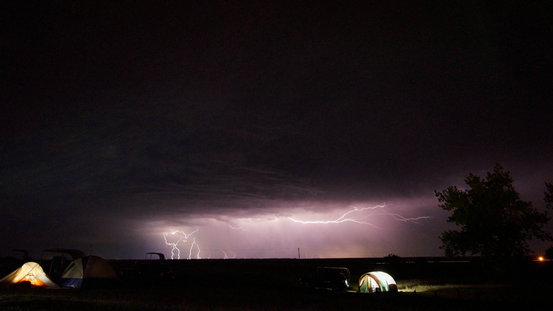 Tents in a thunderstorm at night with lightening in the sky.