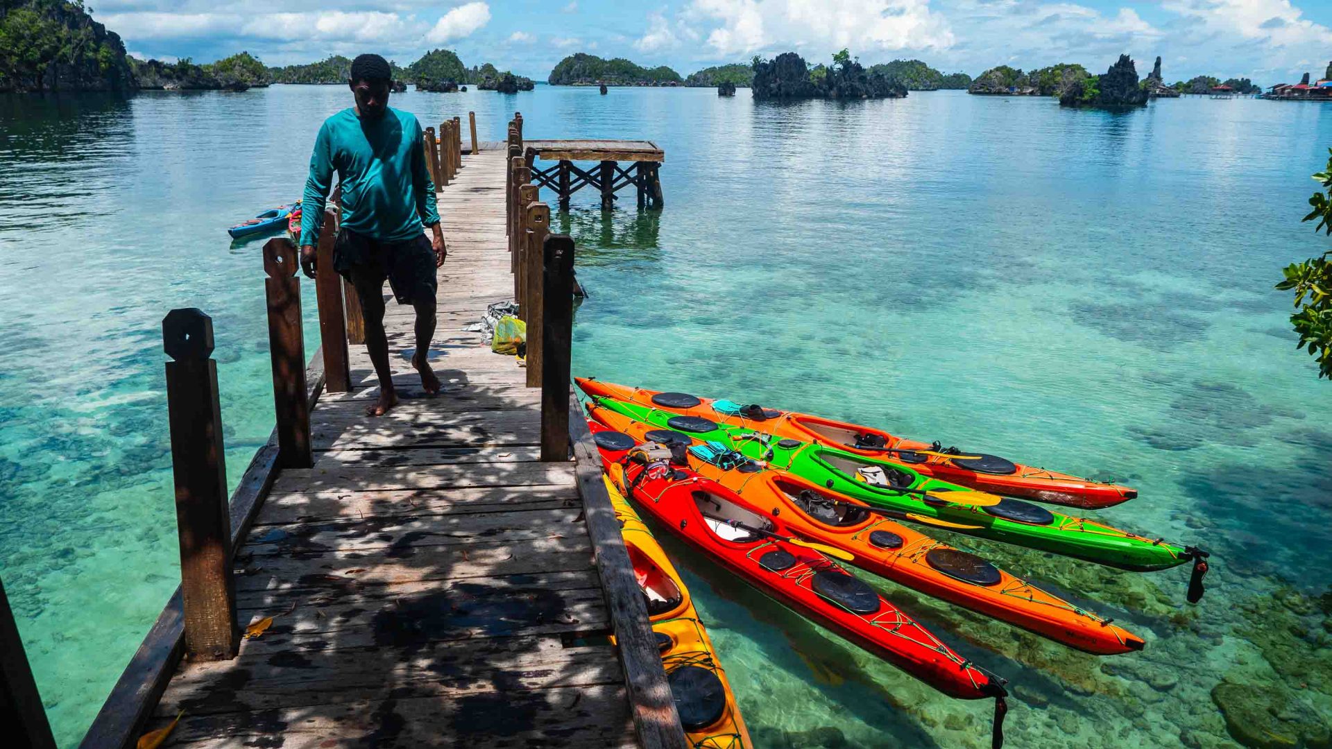 A man walks past some colourful kayaks which are moored.