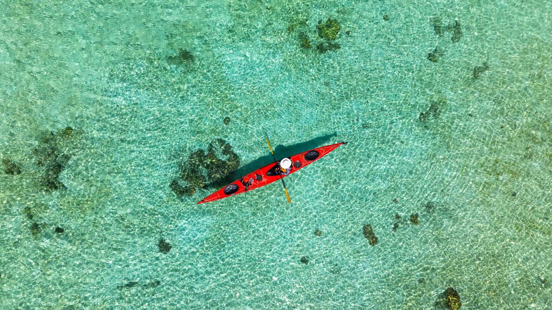 A drone photo of a red kayak in turquoise water.