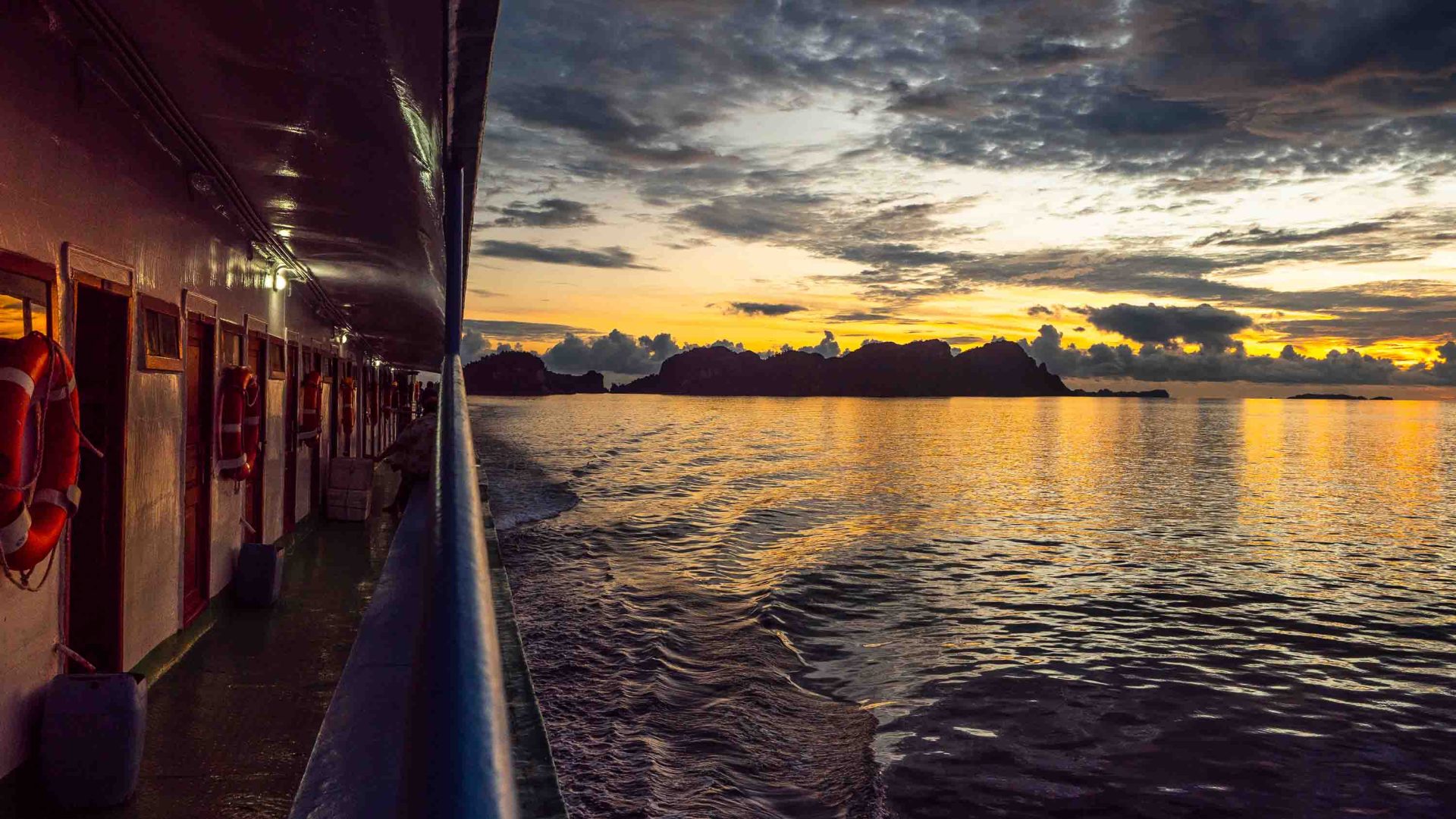 The side of a ferry as it makes its way through the water at sunrise.