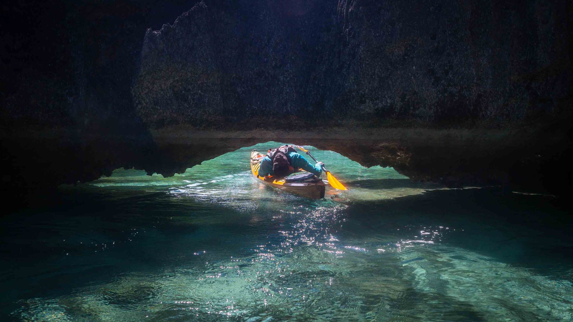 Usman ducking under a rocky arch in a kayak.