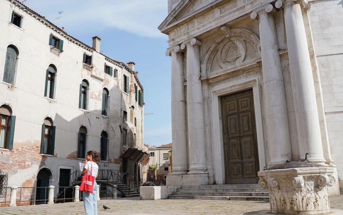 A guide looks at a piece of paper while standing in the middle of a square/piazza in Venice