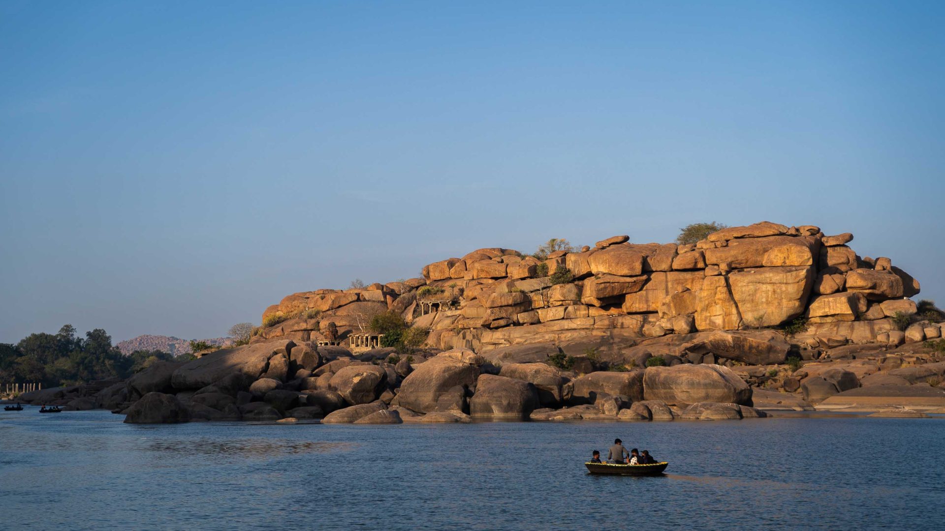 A boat crosses a body of water with rocks in the background.