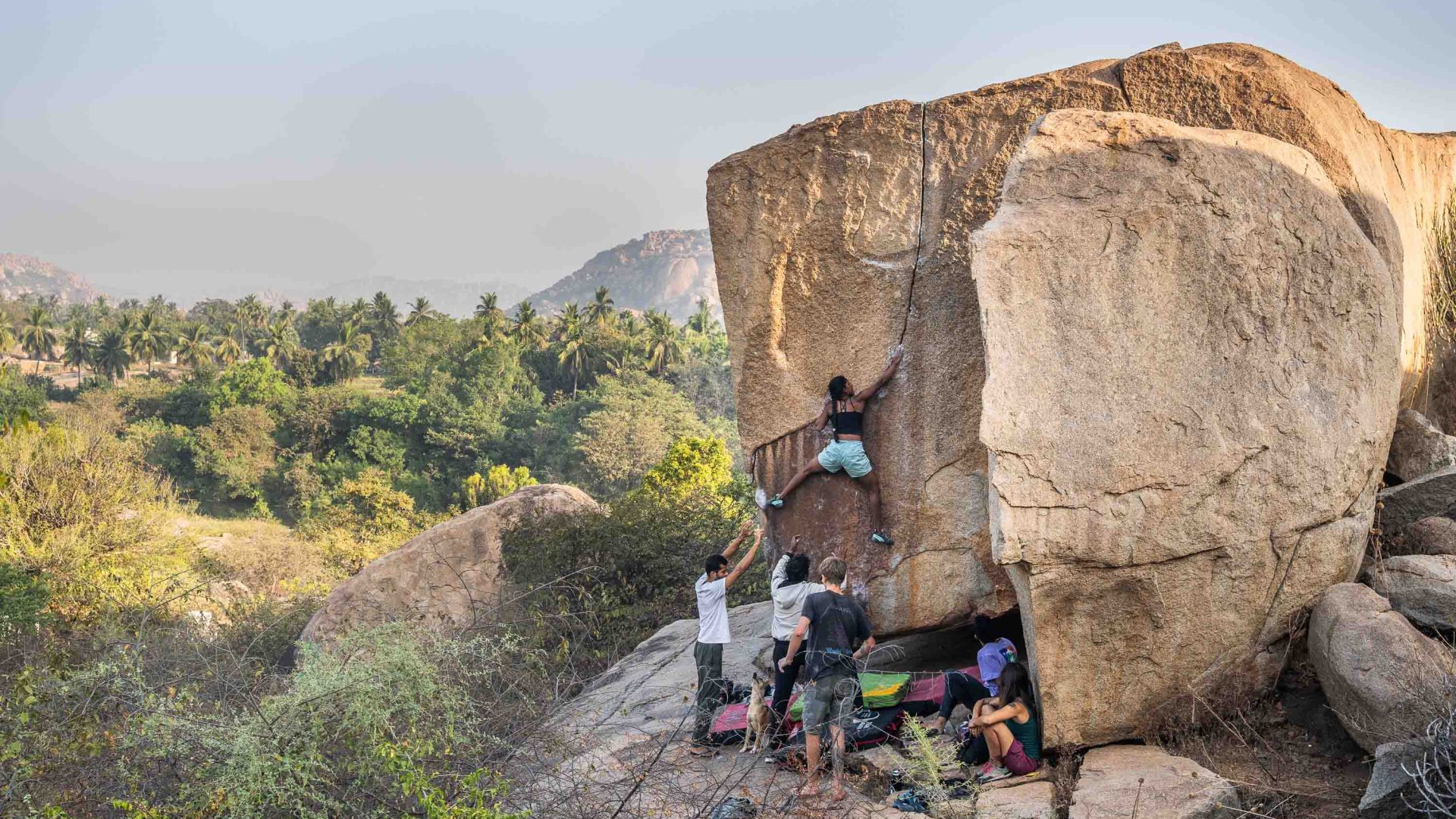 A group of people assists a woman to climb a boulder.