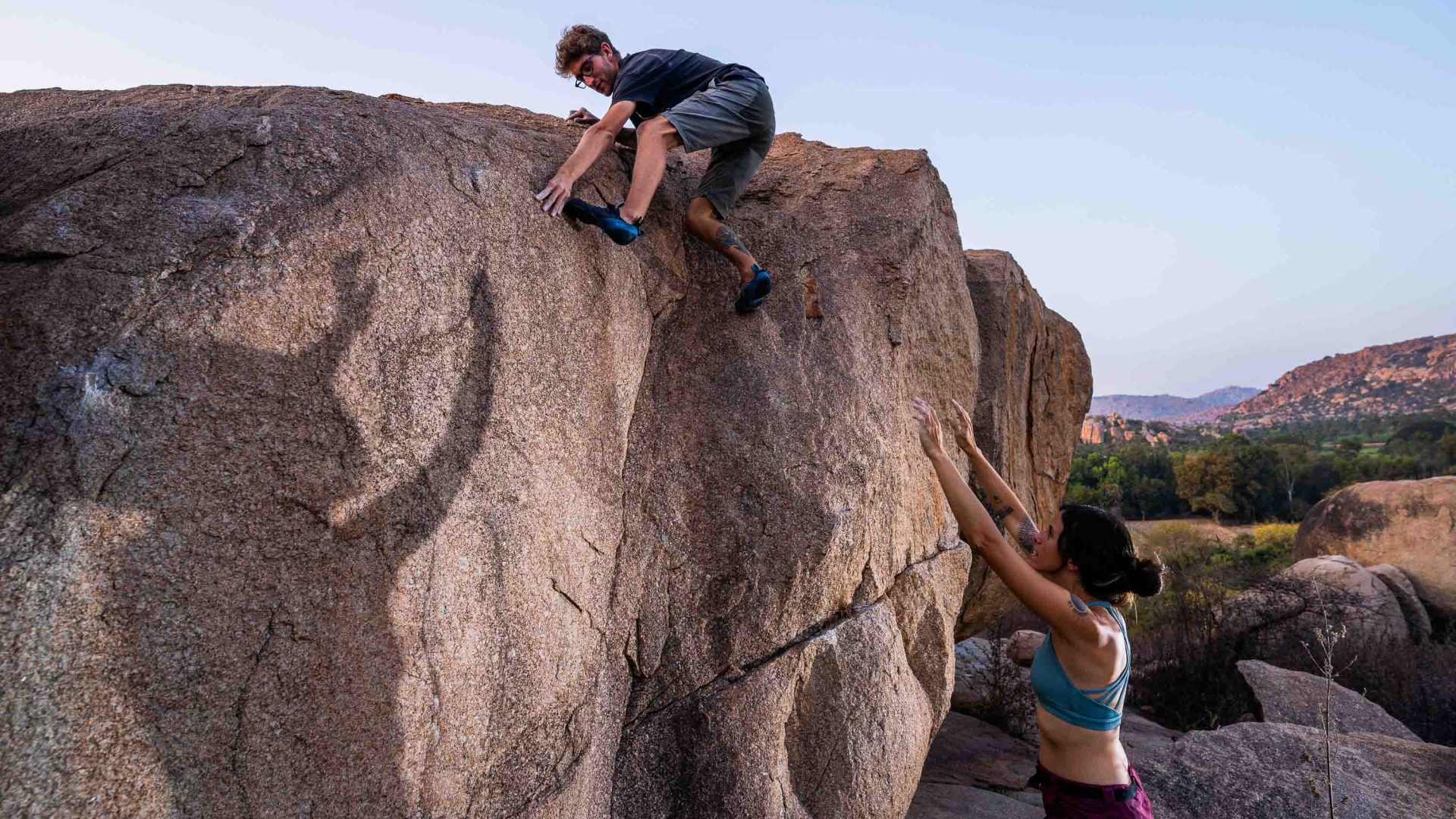 A woman helps a man to climb a boulder.