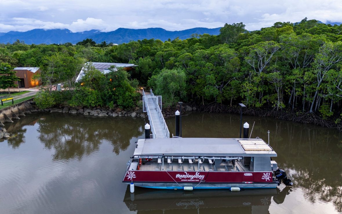 A boat passes through a brown river with forest on both sides.