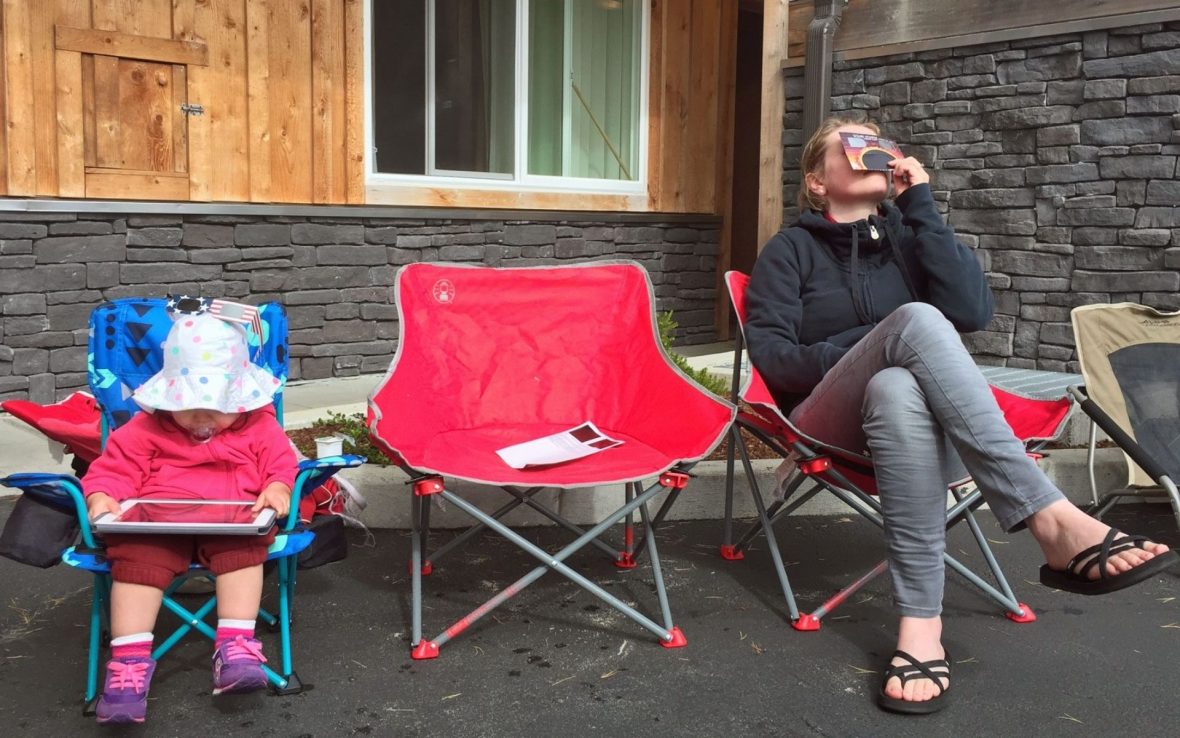 A woman sits in a camping chair wearing eclipse glasses