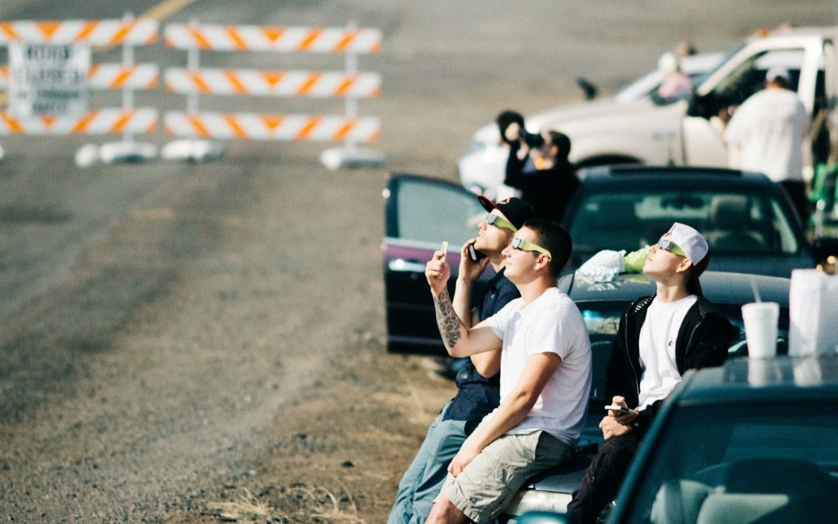 A group of friends leaning on their cars wearing eclipse glasses and looking up