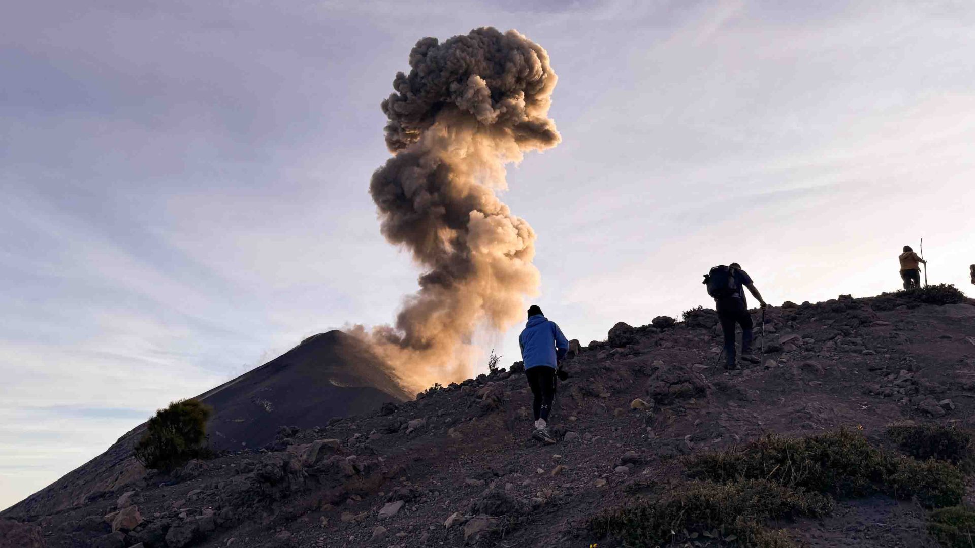 Travelers hike up Fuego as plumes of smoke rise from its crater.