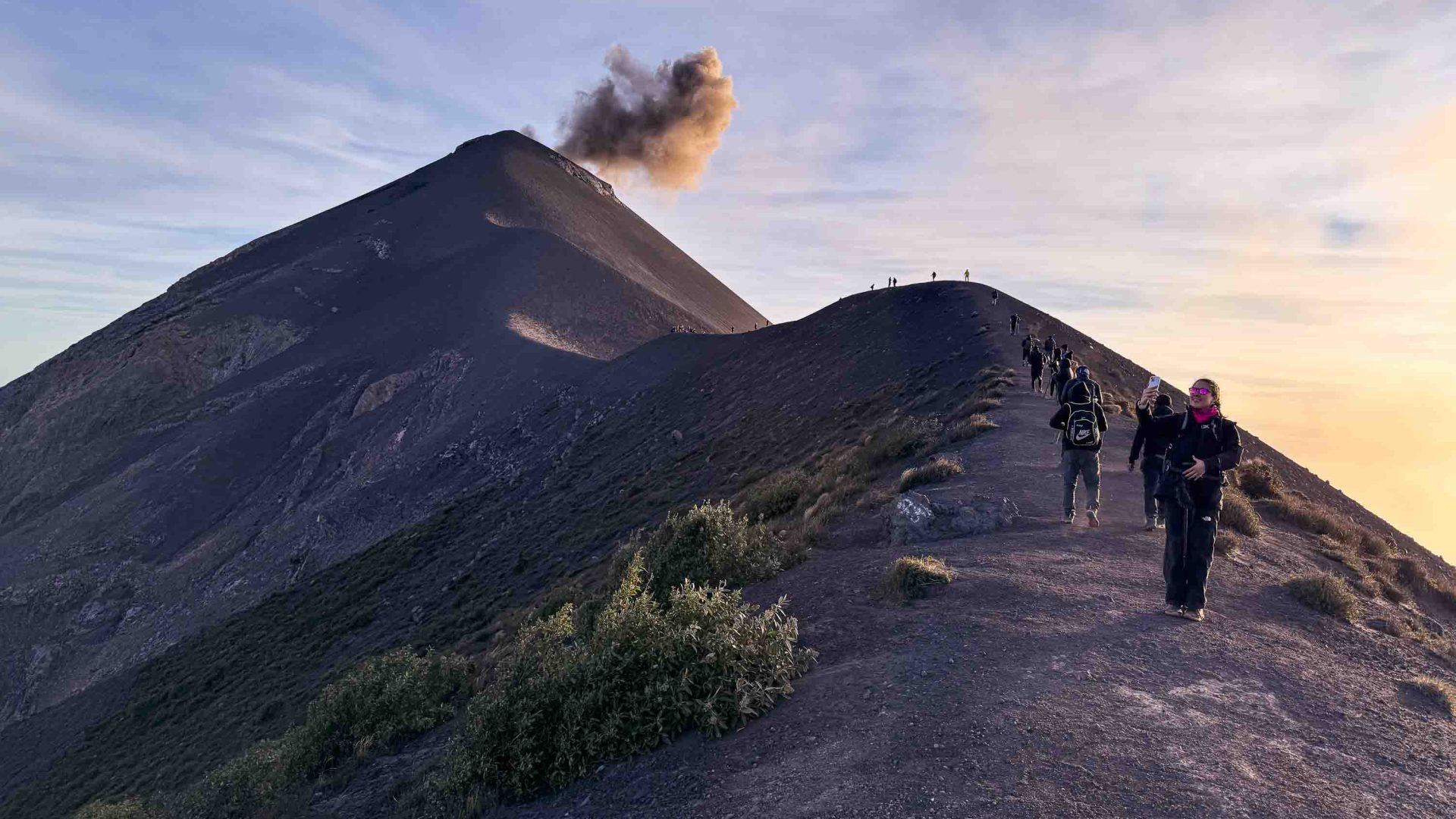 Travelers hike up Fuego as plumes of smoke rise from its crater.