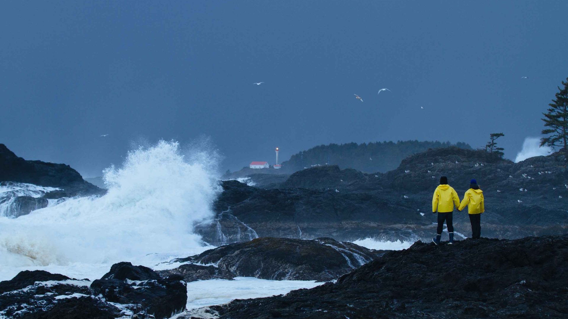 A couple of people look out at the grey day from some rocks.