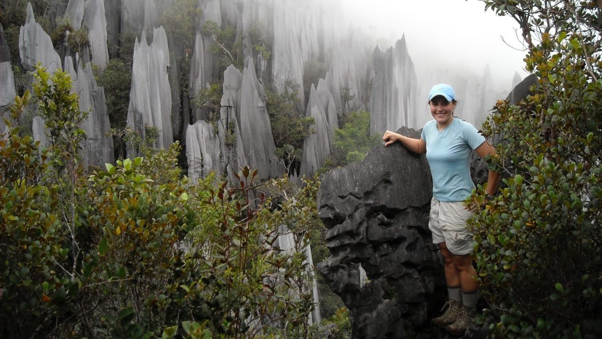 A woman stands against a rugged nature backdrop