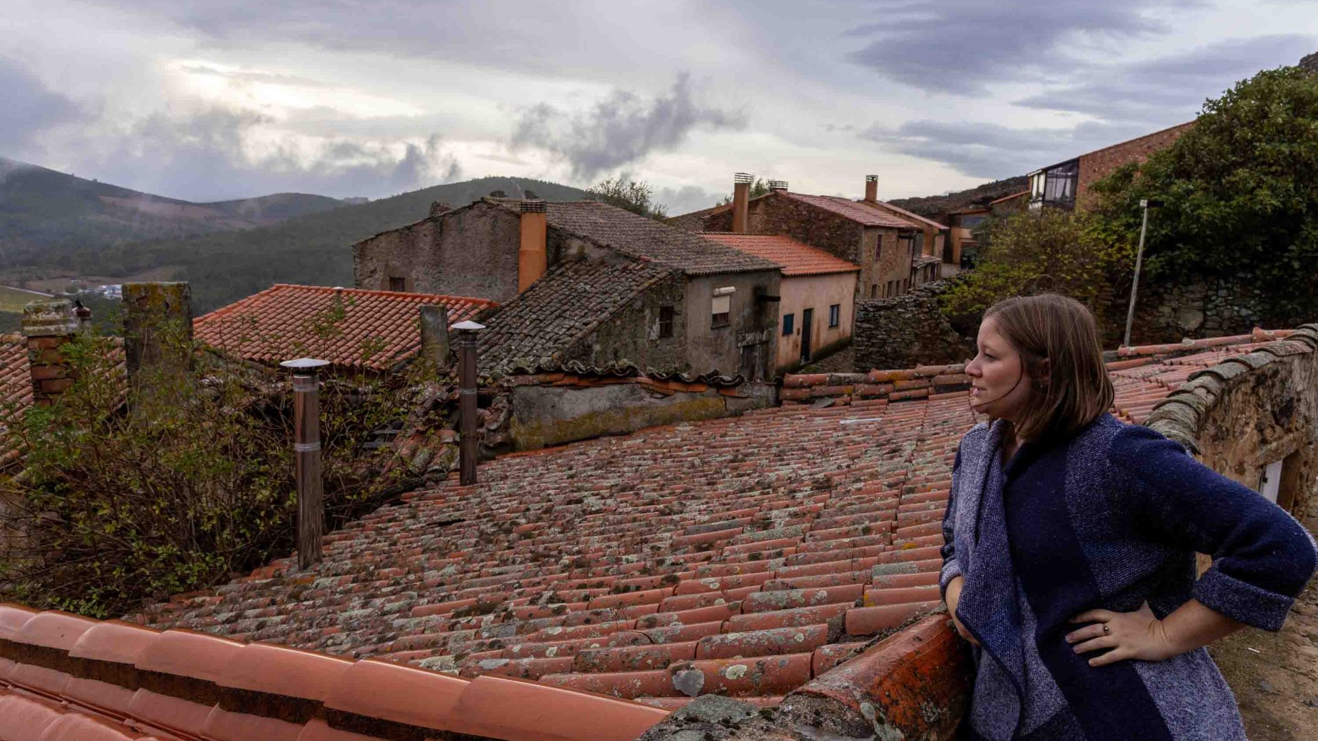 A woman looks out over roof tops and a valley.