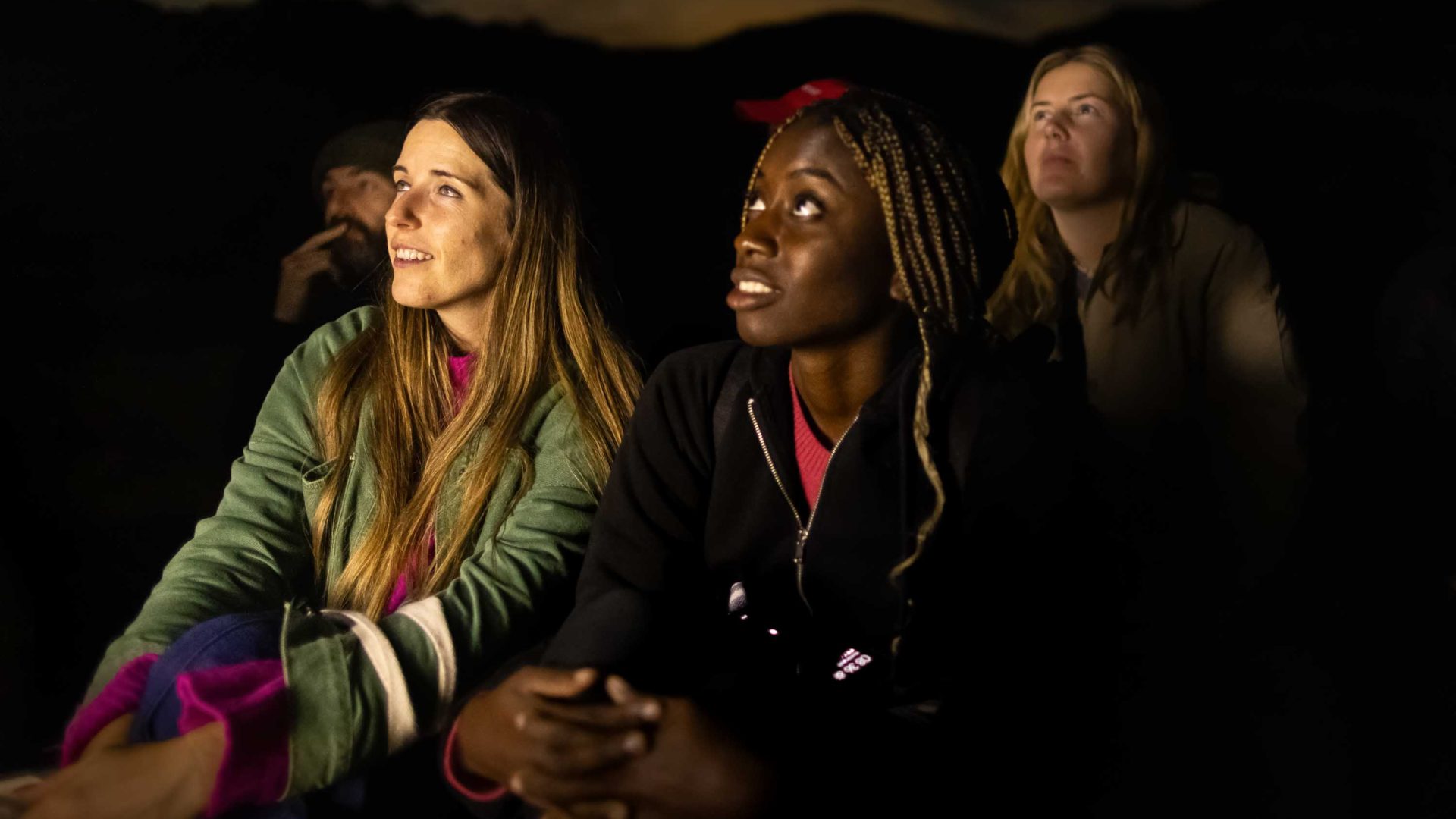 A number of people are lit up by soft light as they watch something.