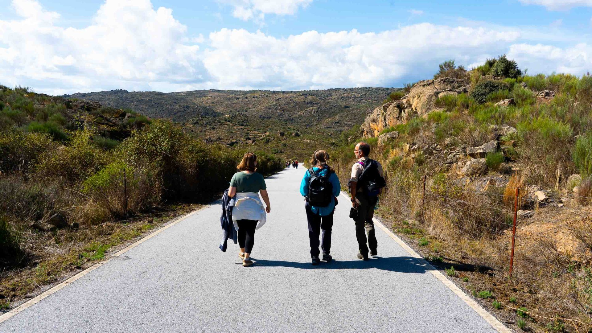 Several people walk down a road which is surrounded by mountains.