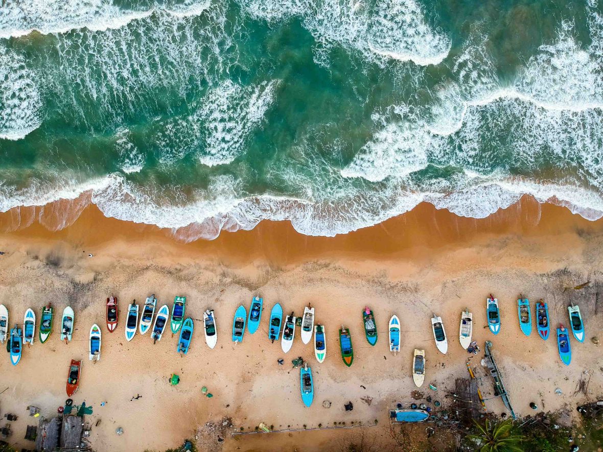 An aerial view of boats on the sand of a beach with waves.