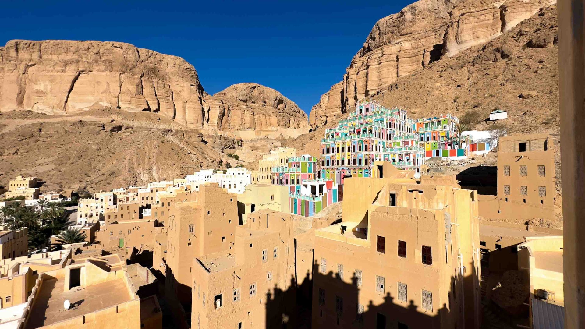 A town surrounded by dry mountains has a colourful cluster of buildings in the centre.