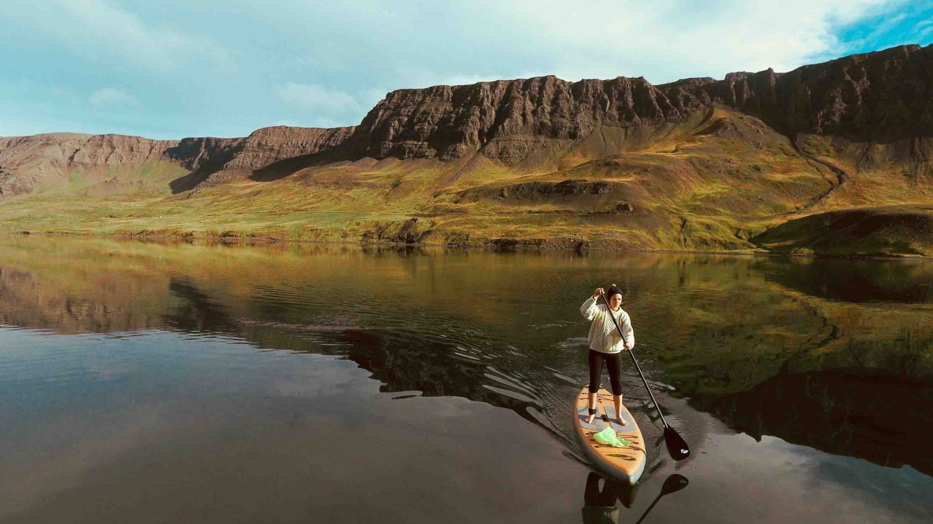 A woman on a stand-up paddle with an arid landscape behind her.