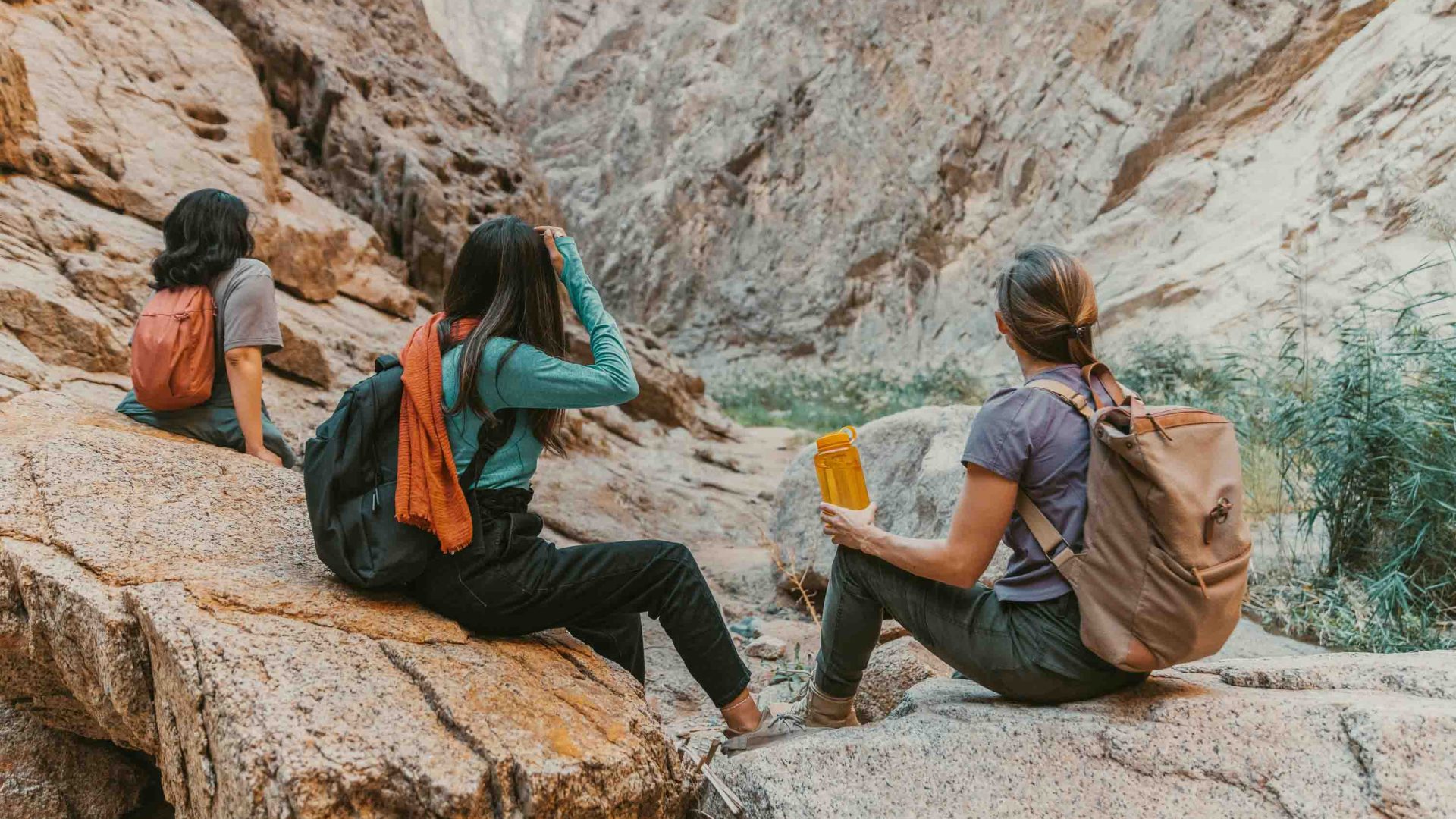 Three women sit and rest while in a rocky valley.