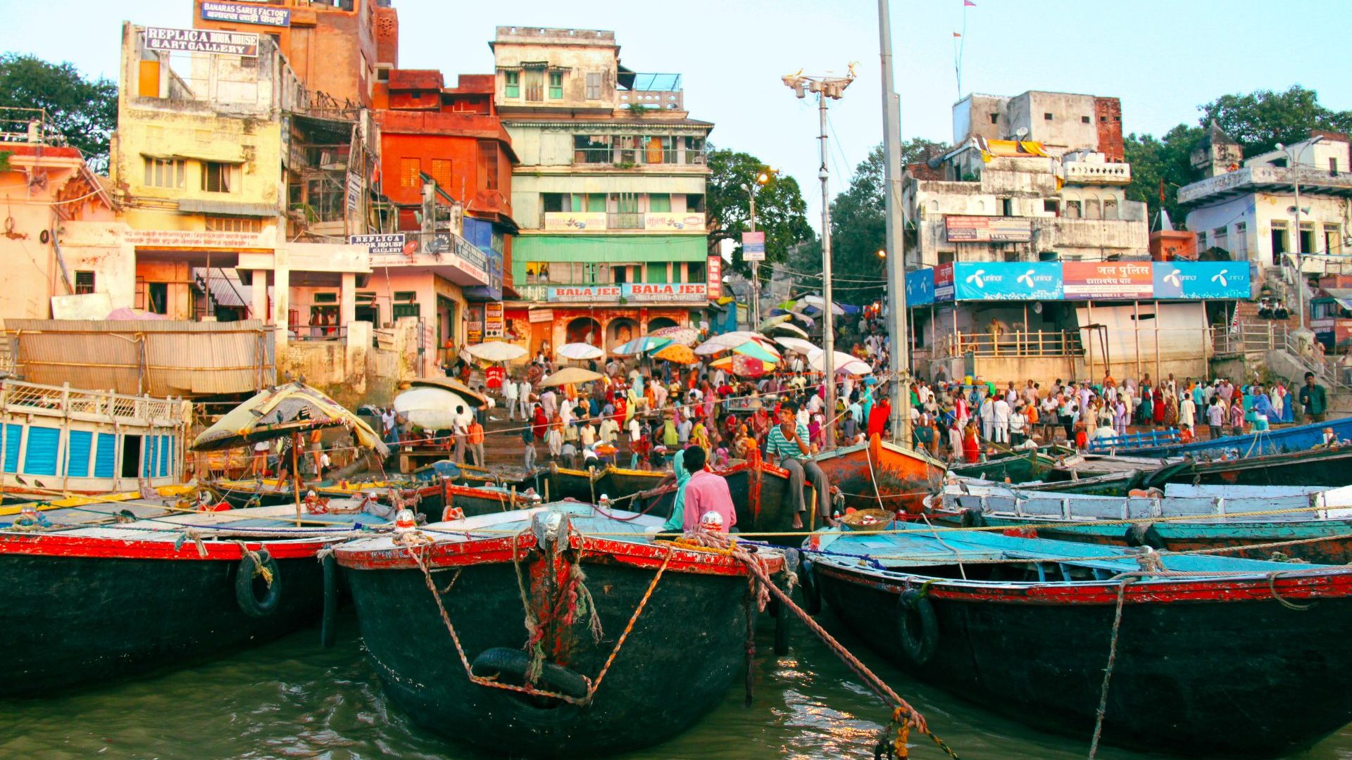 Colorful buildings, a throng of people and boats beside a ghat (steps) on the Ganges River.