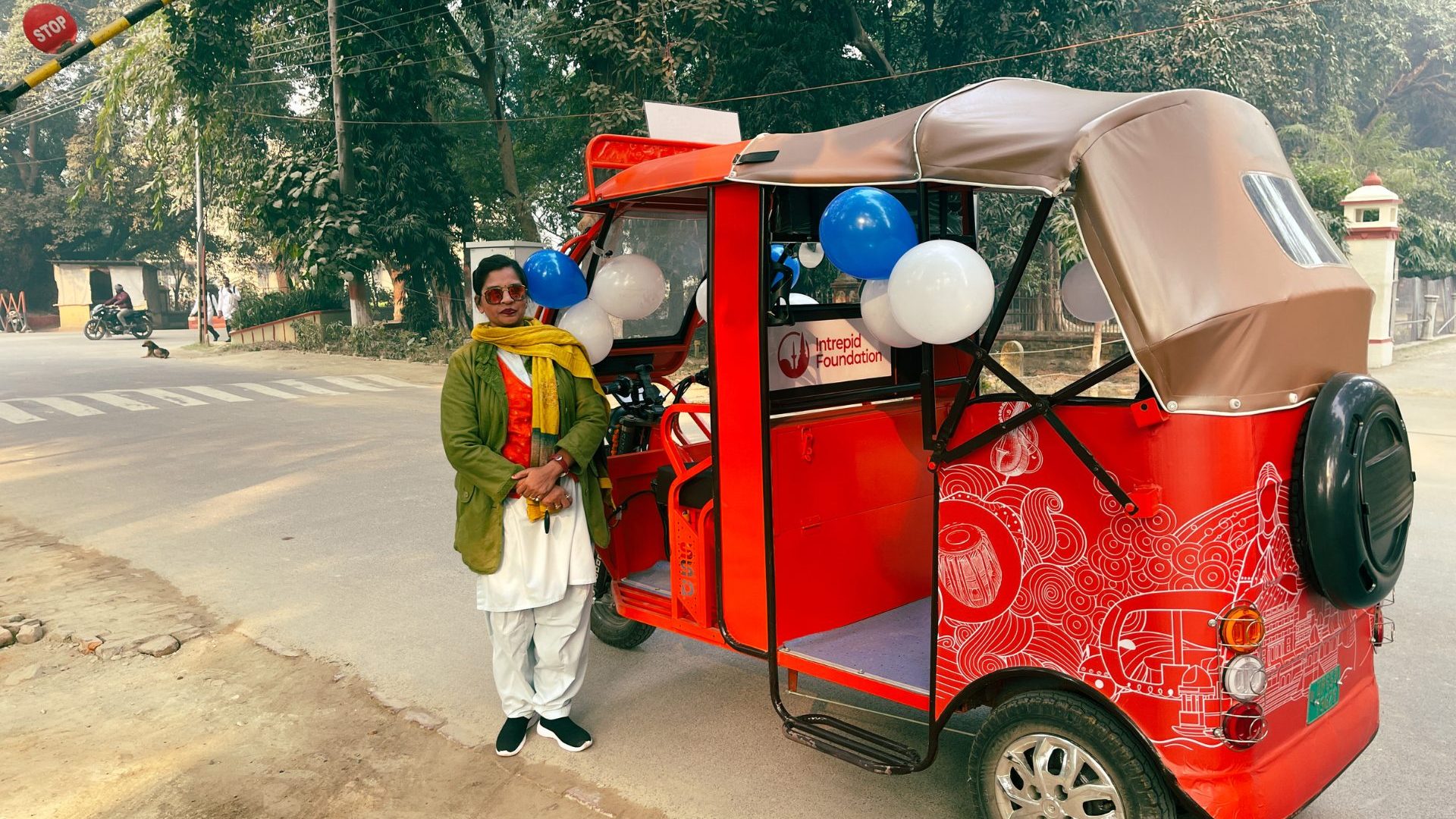 A woman stands beside a red electric rickshaw.
